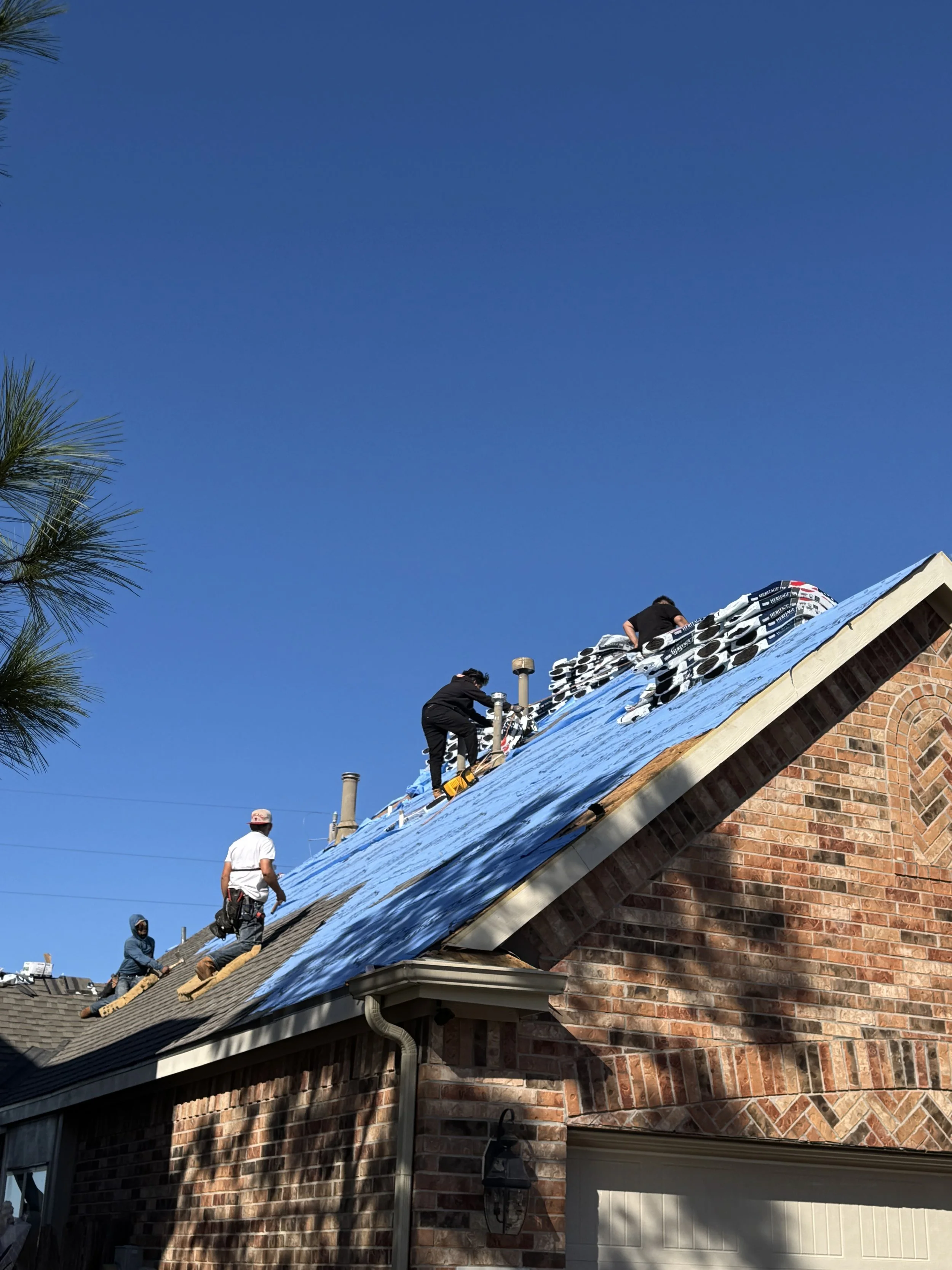 Roofers working on a brick house with blue underlayment