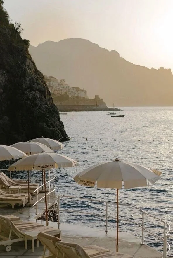 Wedding Website Design, Digital Wedding Stationery, Web Design and Branding for Wedding Professionals | Avelã White. Seaside view with umbrellas and lounge chairs next to the ocean, rocky cliffs, and distant mountains.