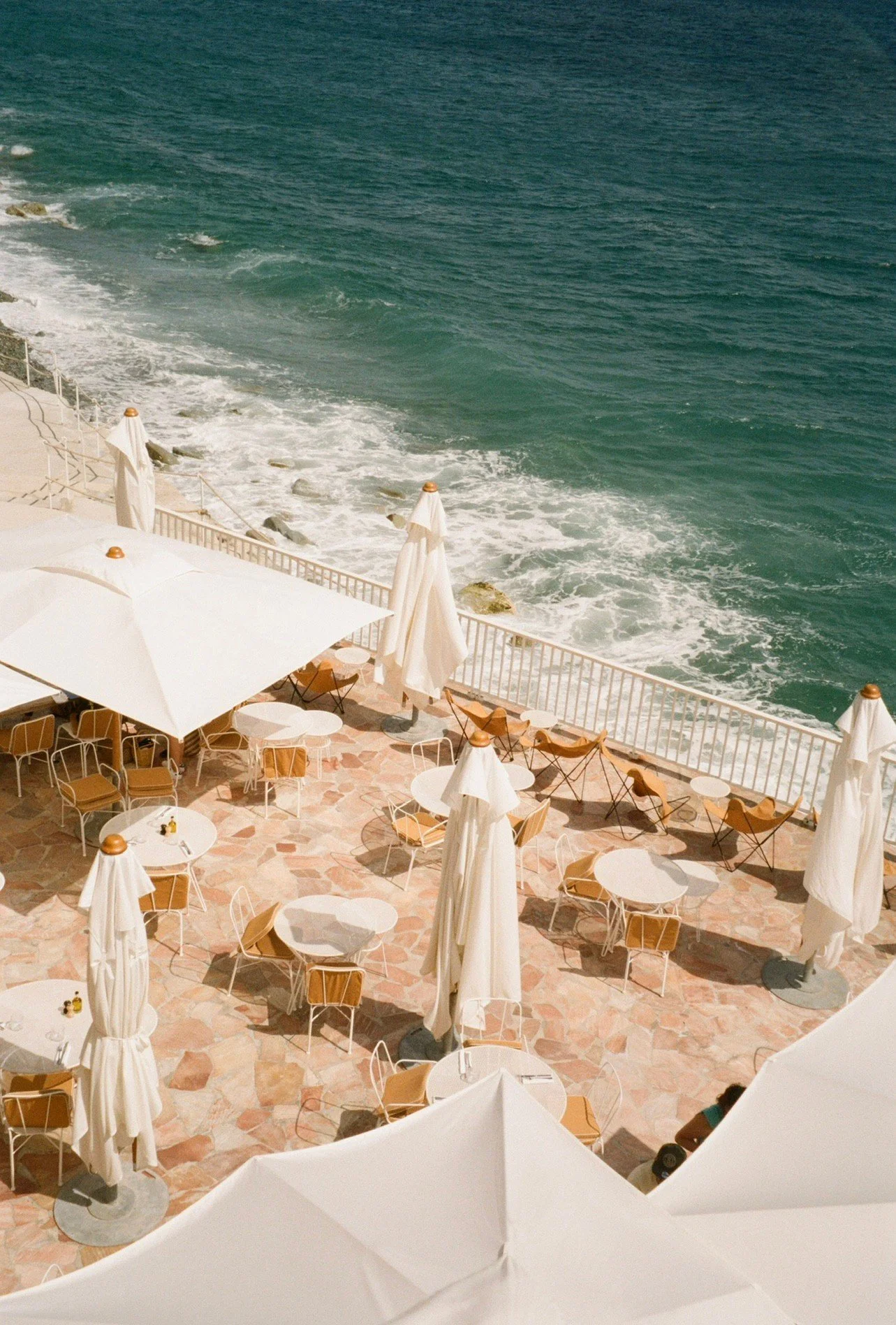 Wedding Website Design, Digital Wedding Stationery, Web Design and Branding for Wedding Professionals | Avelã White. Outdoor seaside cafe with white umbrellas, tables, and chairs, overlooking ocean waves.