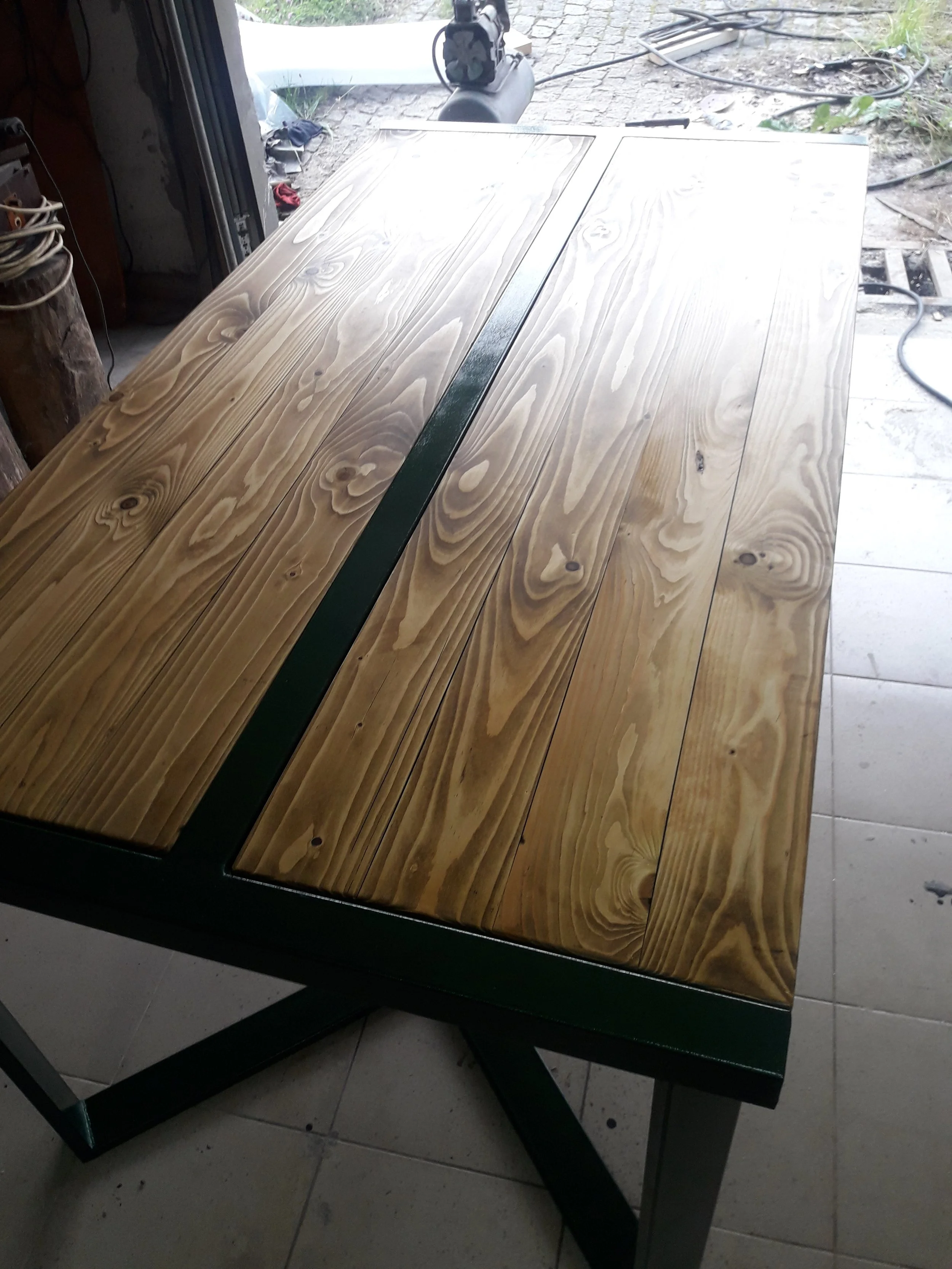 Wooden table with metal frame and legs in a workshop setting.