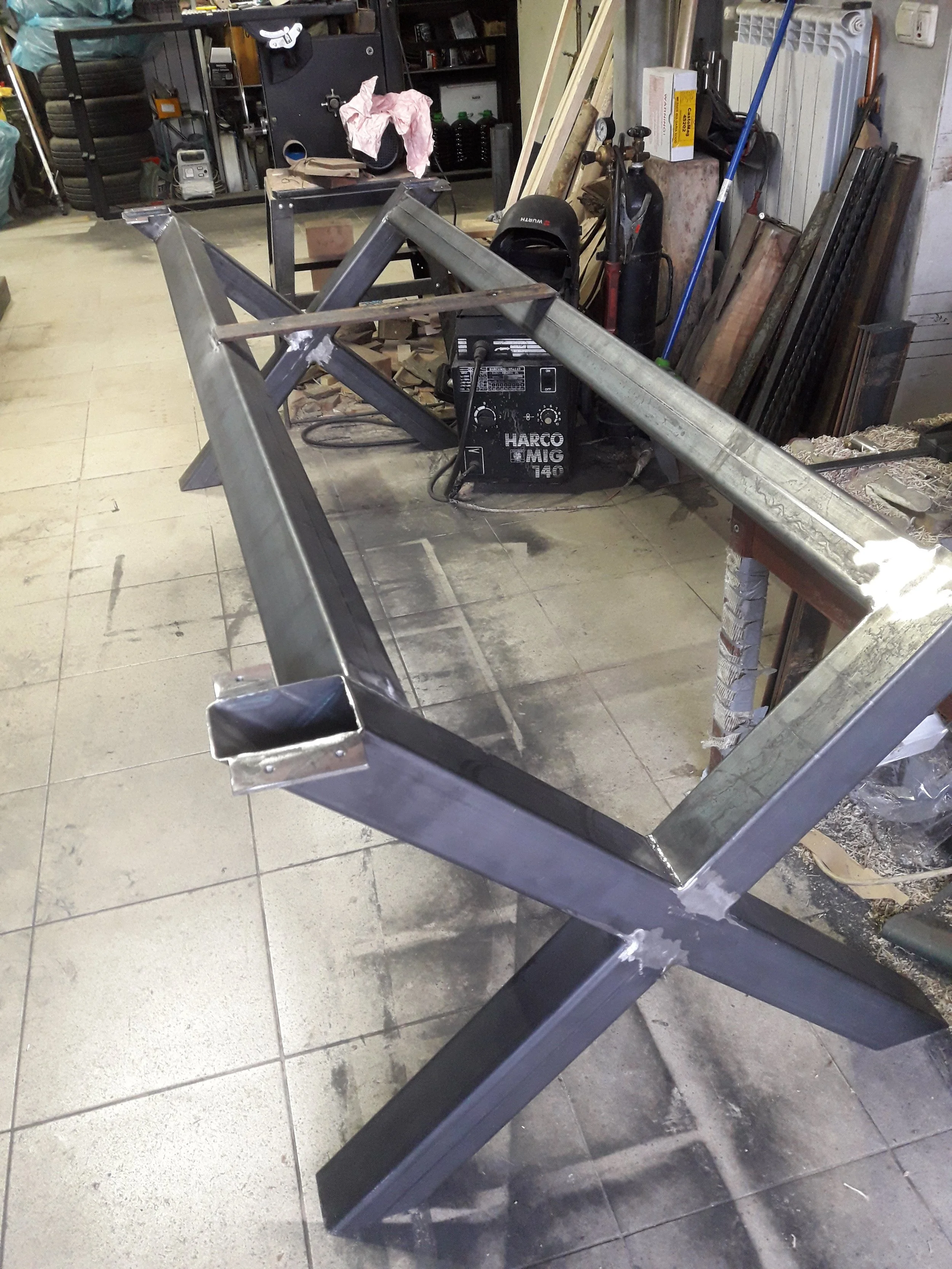 Workshop with metal frame structure being built on tiled floor, surrounded by tools and equipment.