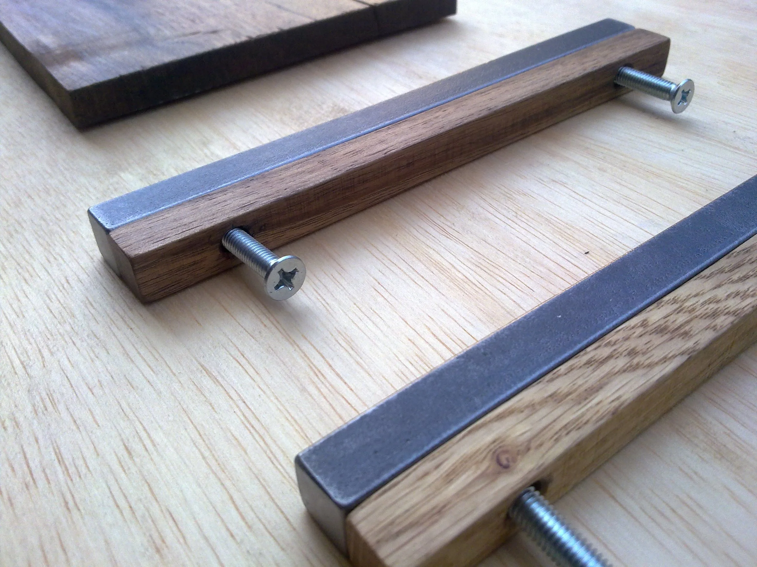 Two wooden handles with metal bars and screws, placed on a wooden surface.