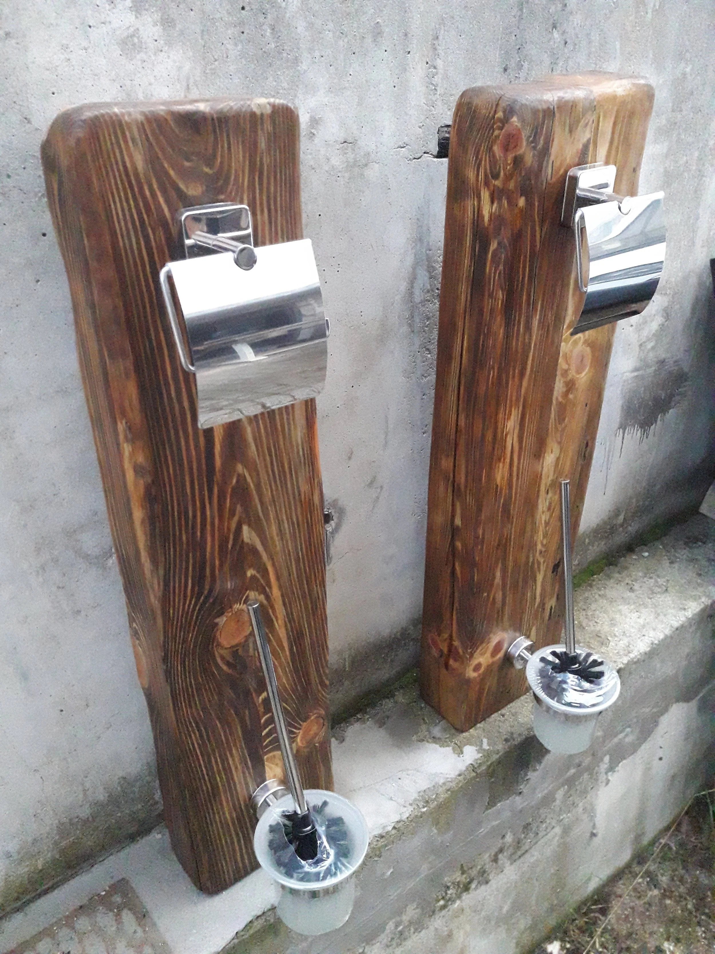 Two wooden panels attached to a concrete wall with mounted toilet paper holders and toilet brushes in holders.