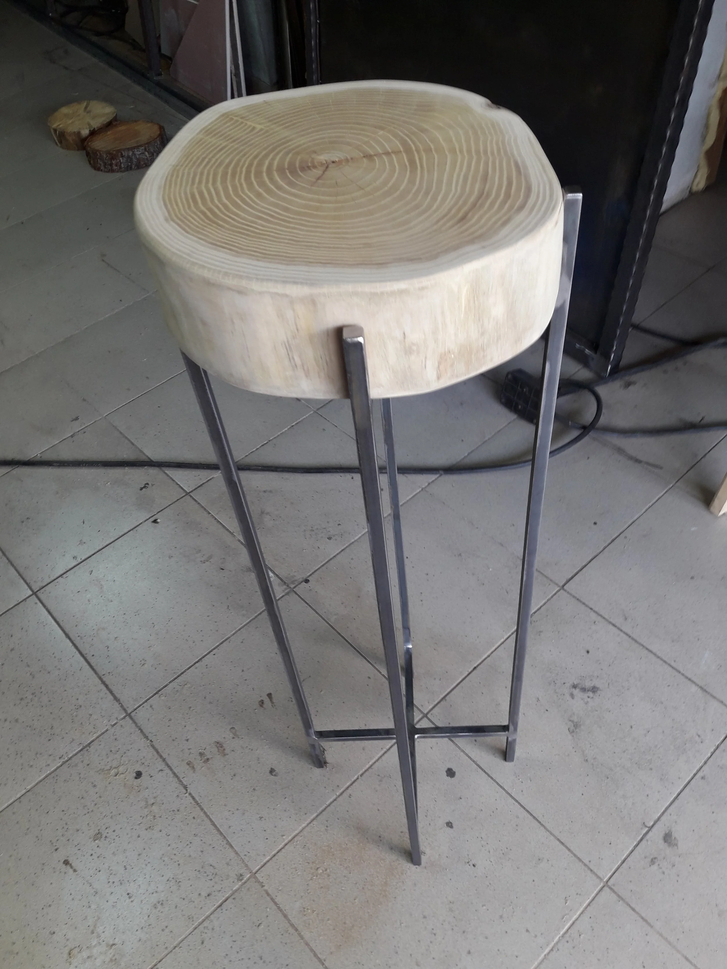 Metal-legged table with a wooden, round cut tabletop placed outdoors on tiled flooring