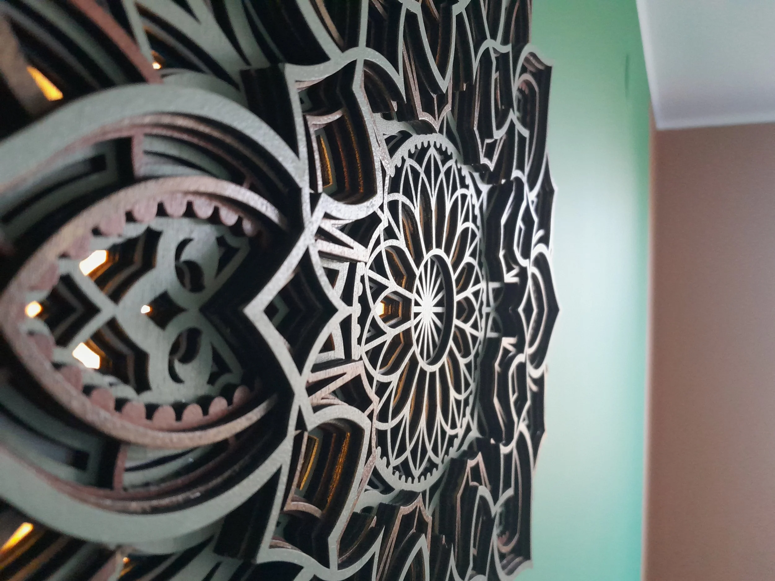 Intricate layered wooden mandala artwork on a green wall