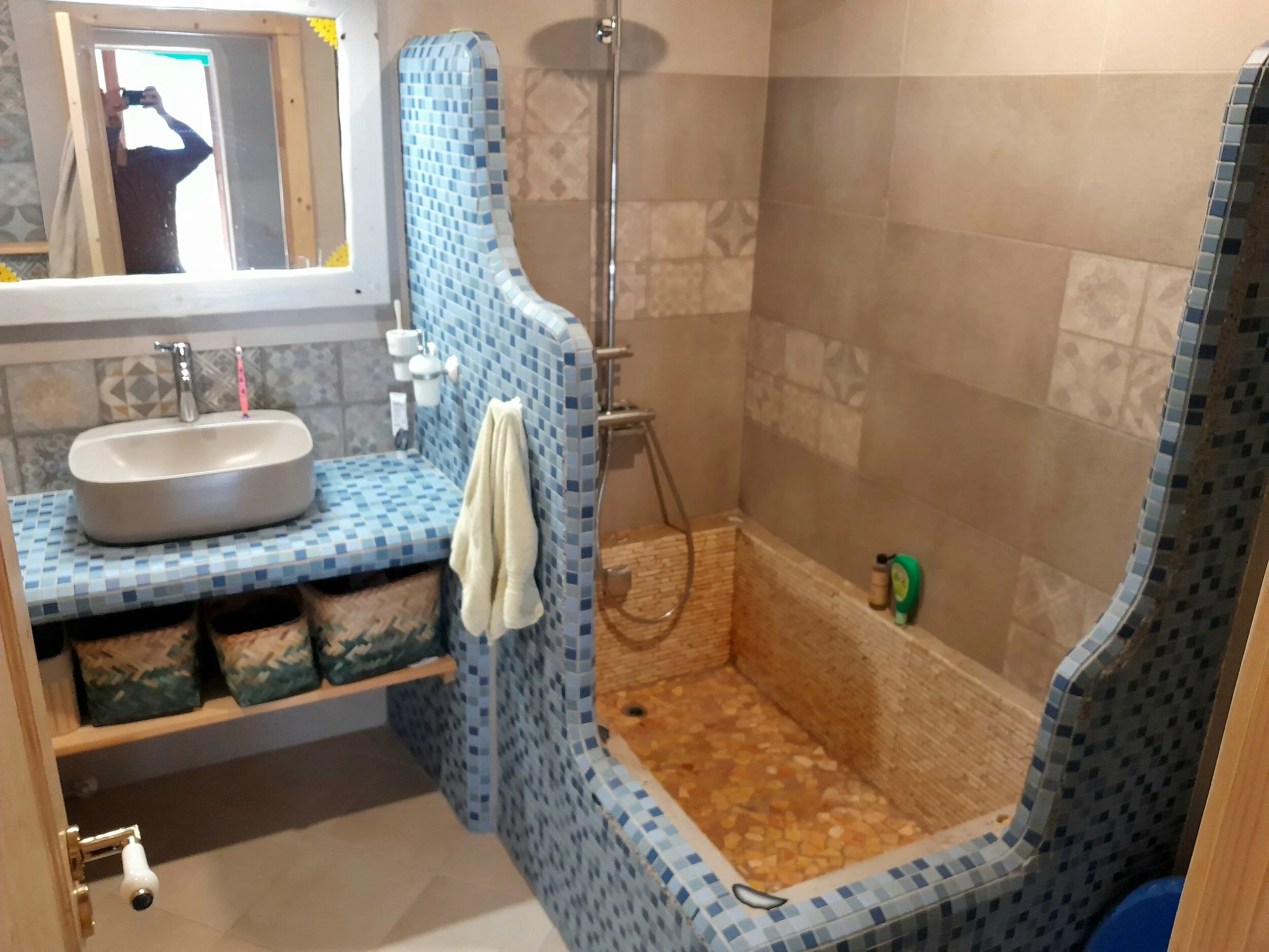 Bathroom with mosaic tiled shower and sink, woven baskets under the counter, and a rectangular mirror.