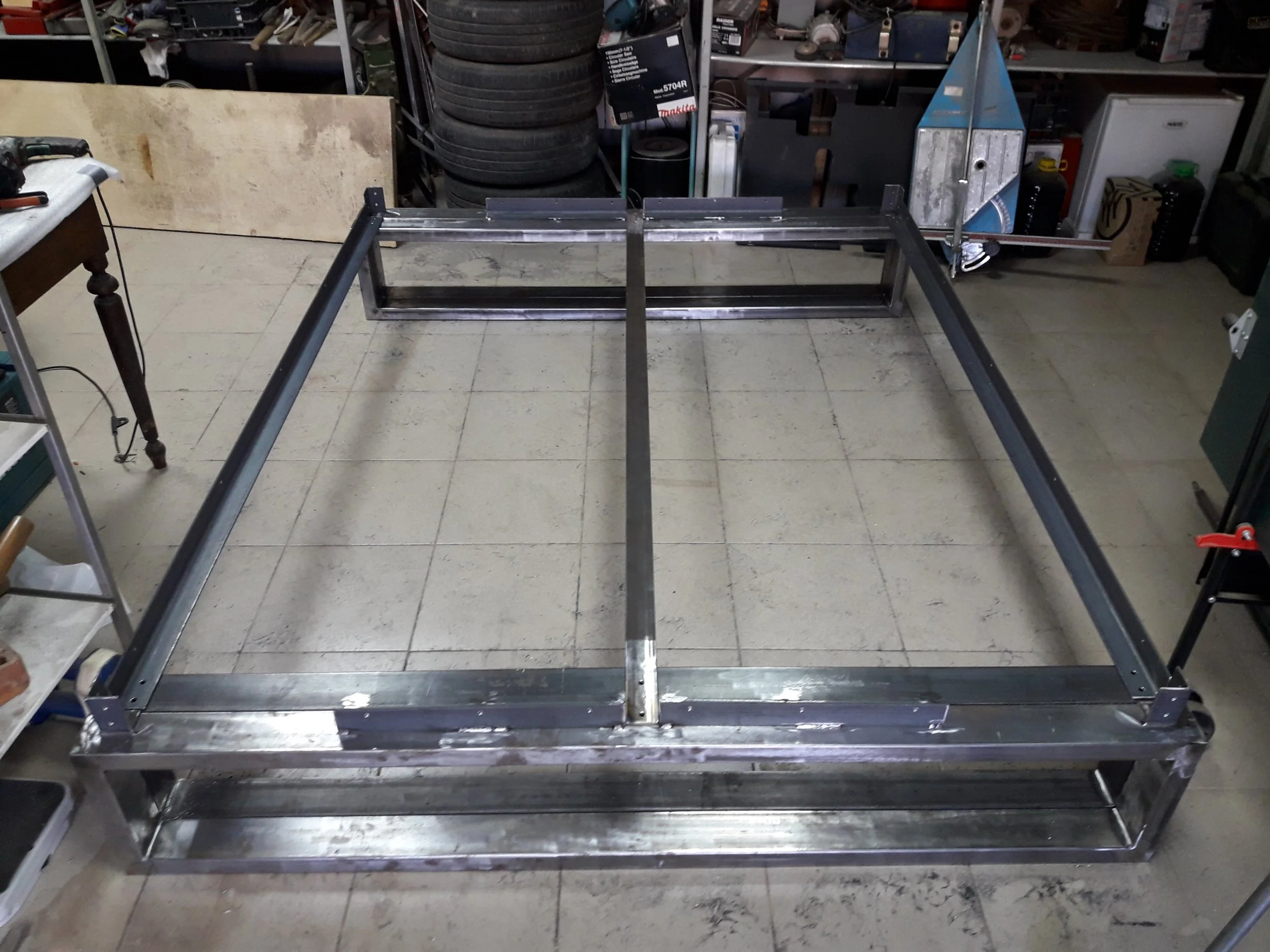 Metal frame structure in a workshop with tools and tires in the background.