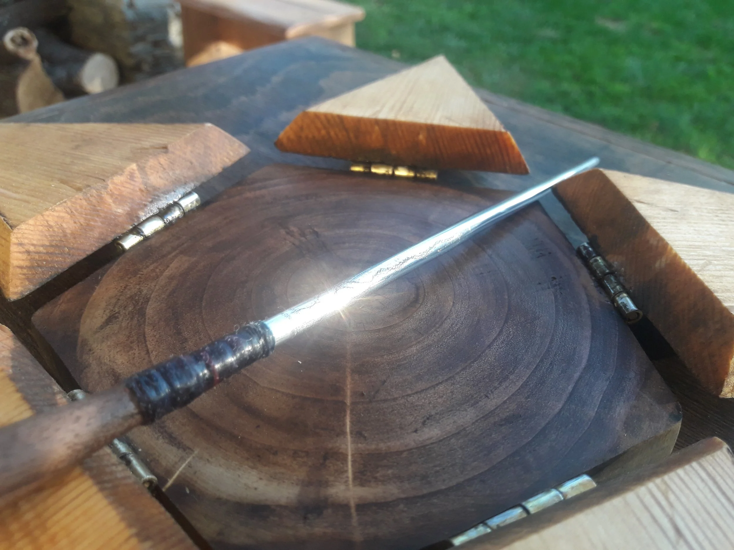 Close-up of a wooden box with a hinged lid and a metal wand resting on it, set outdoors.