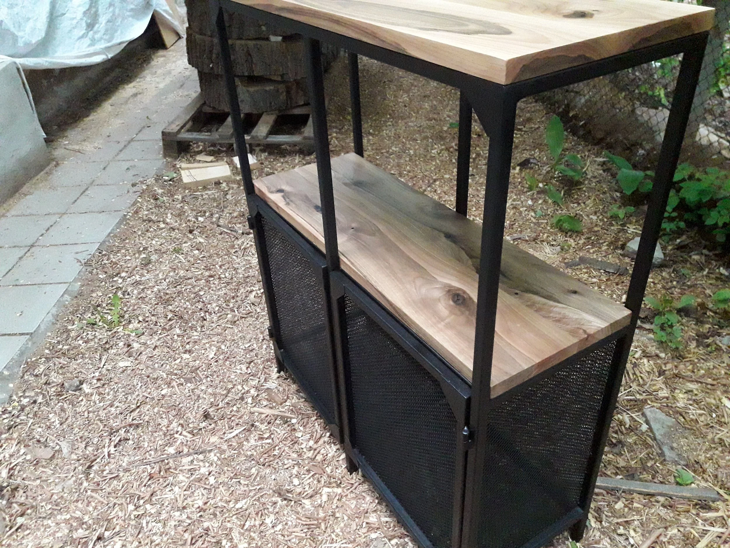 Metal and wood storage unit with mesh panels in outdoor setting