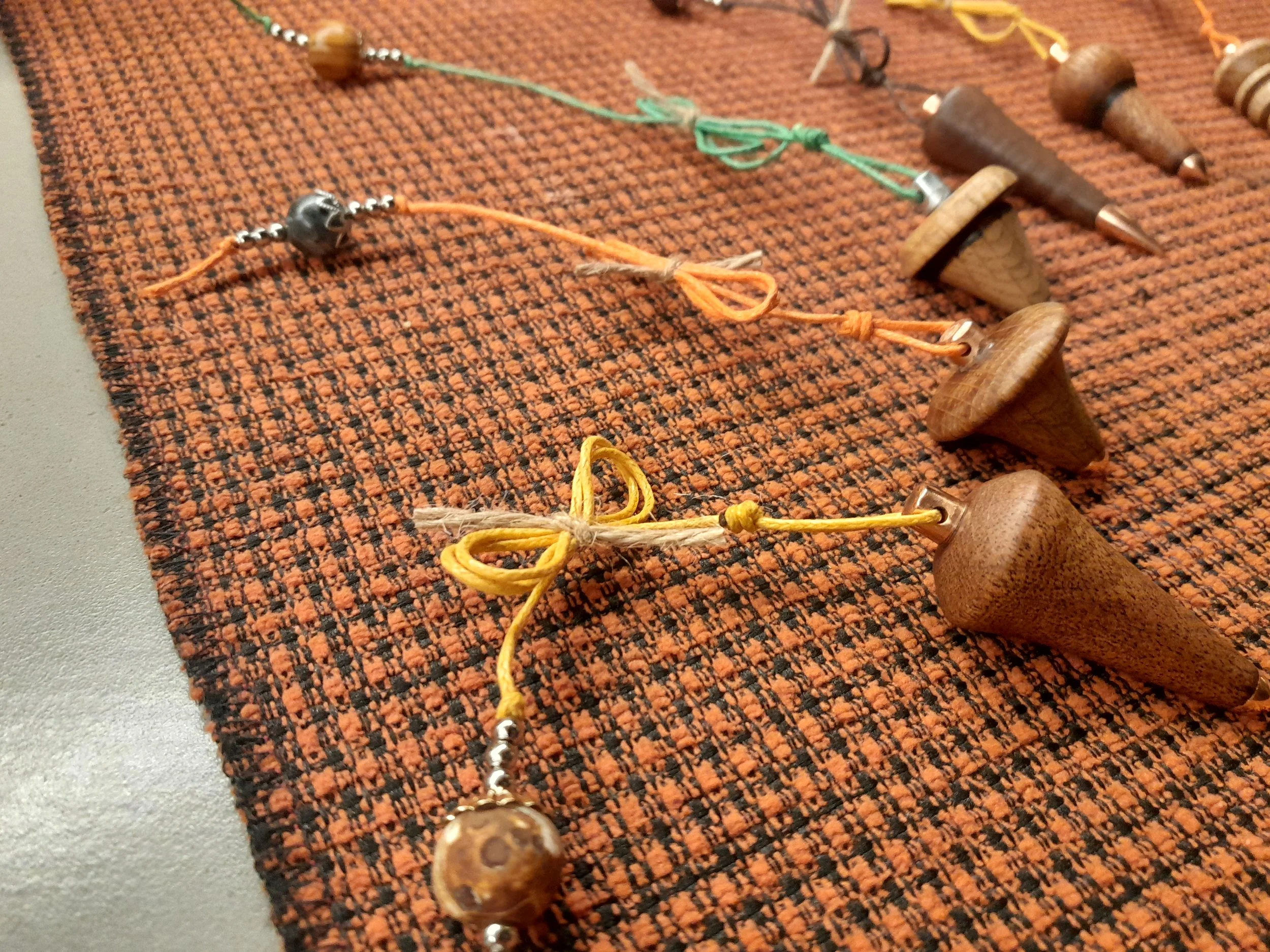 Wooden spinning tops on a woven mat with colorful strings and beads.