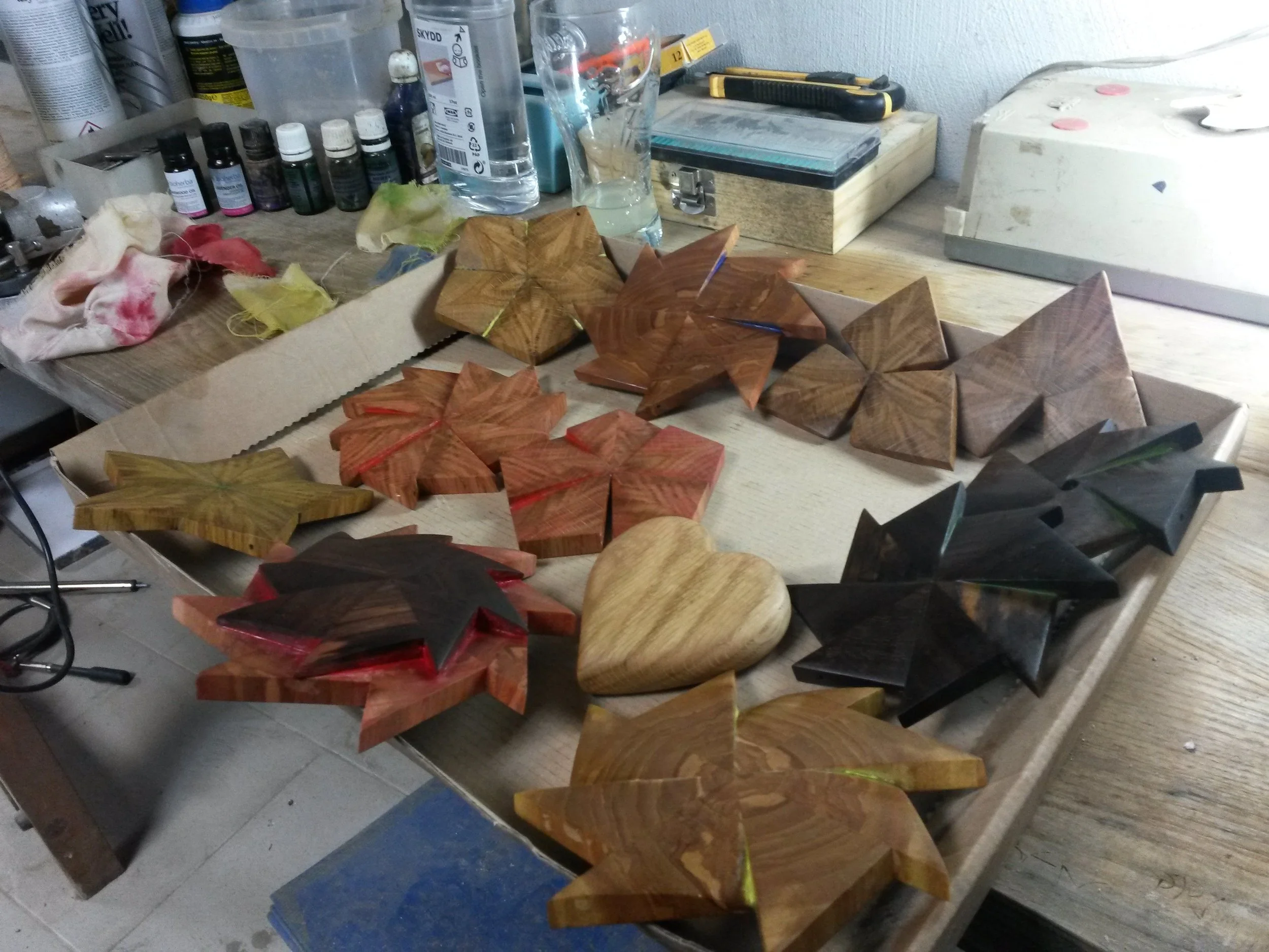 Wooden geometric shapes and heart cutouts on a workbench with various tools and bottles in the background.