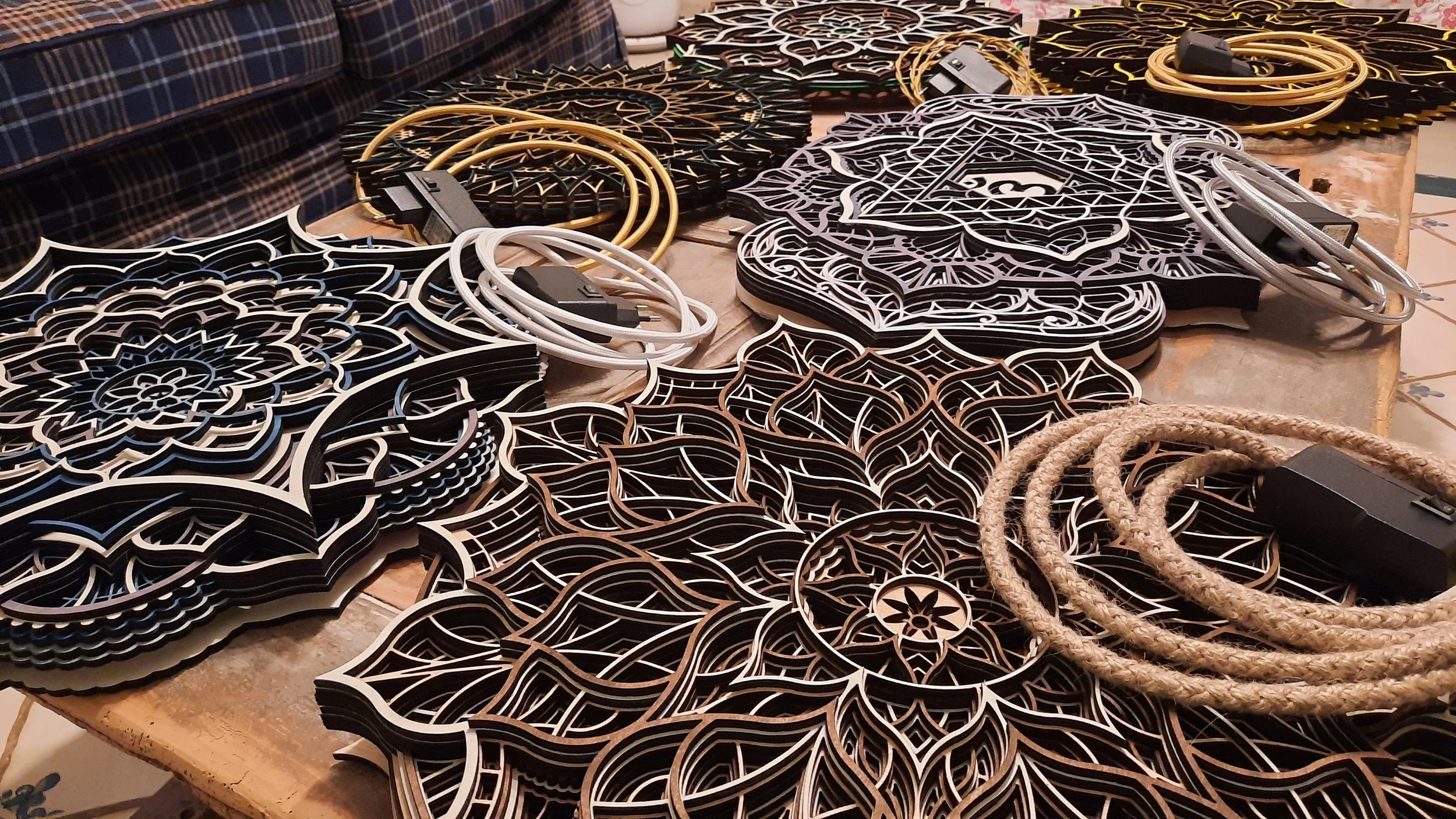 Intricate laser-cut wooden panels with mandala patterns on a table, accompanied by coiled electrical cords.