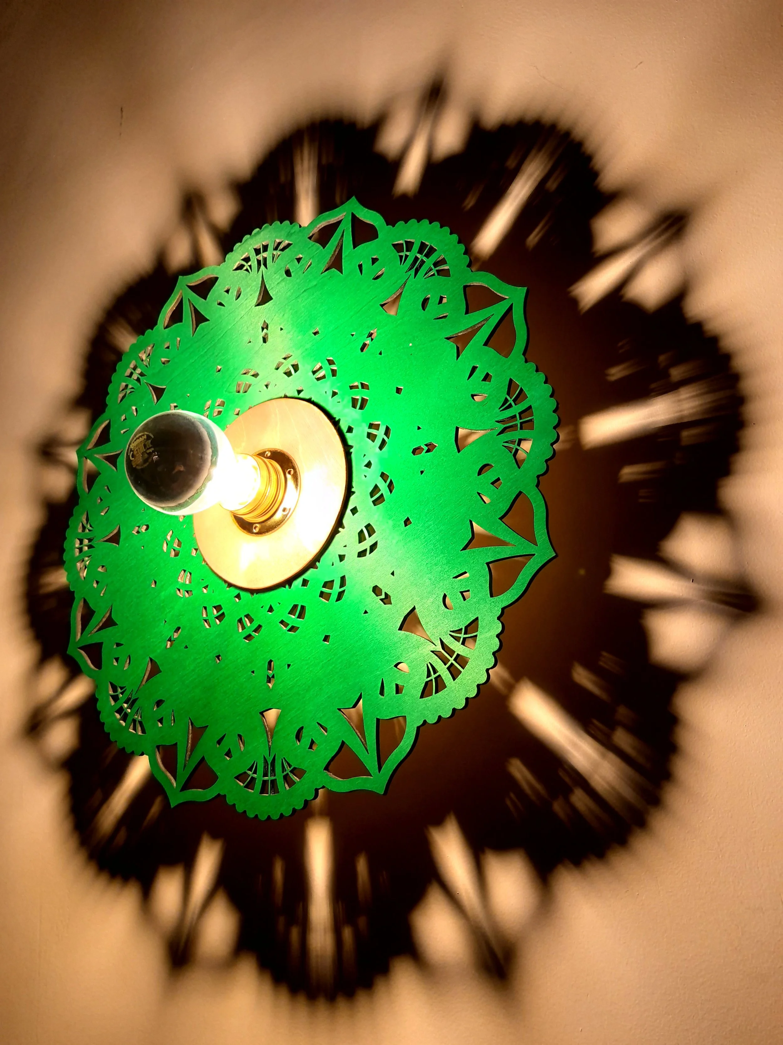 Green decorative wall sconce with light bulb casting intricate shadow pattern on wall.