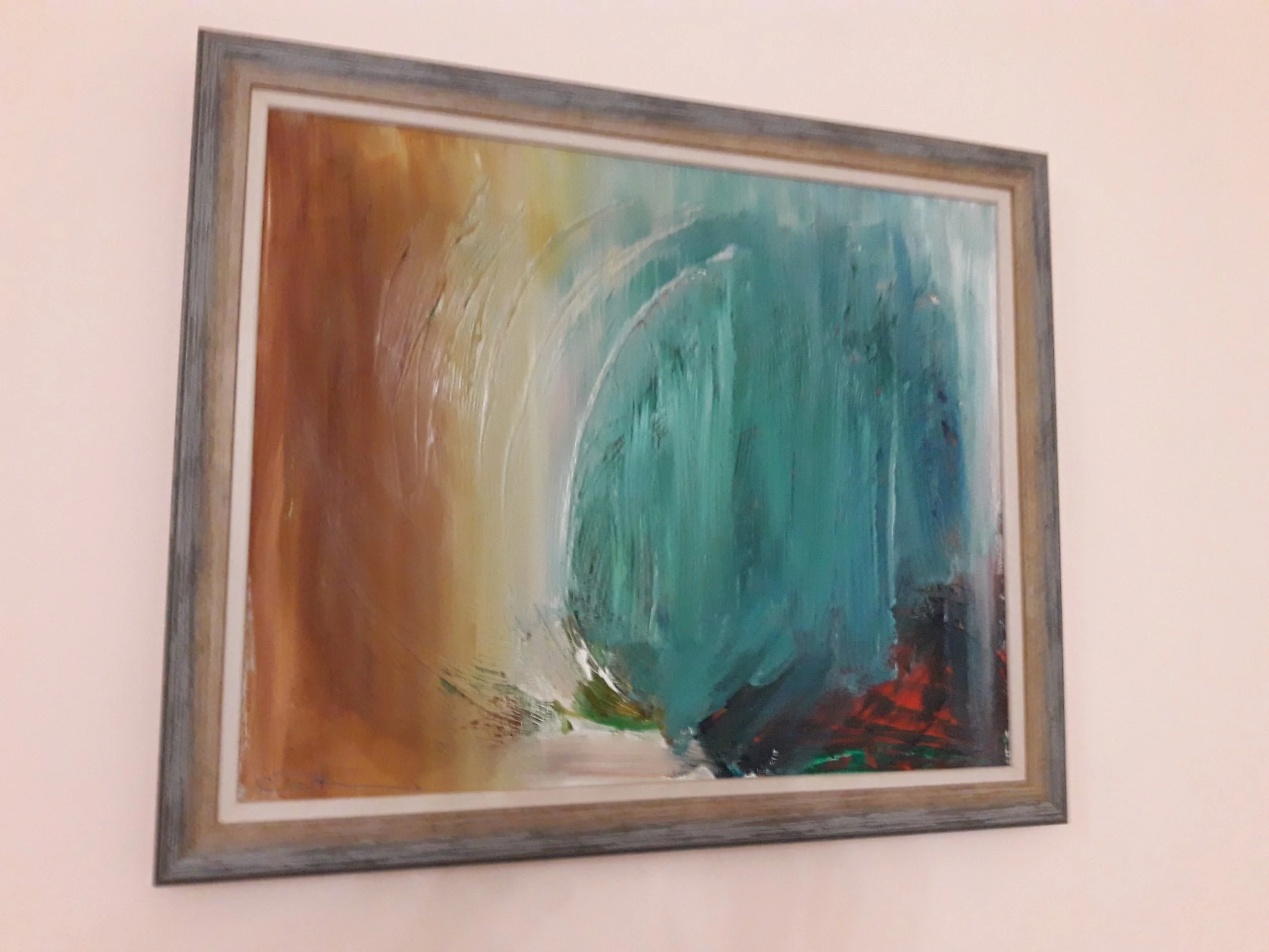 Abstract painting with swirling colors of blue, green, brown, and red, framed in gray, hung on a wall.