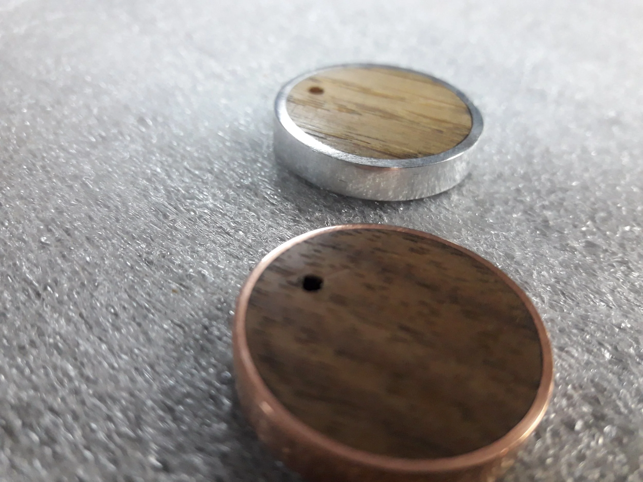 Two circular wooden tokens with metal edges on a textured surface.