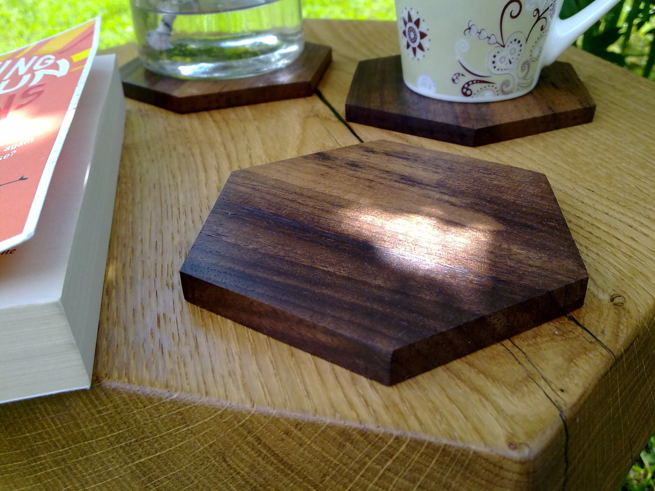 Wooden table with hexagonal coasters, a book, a cup, and a glass of water.