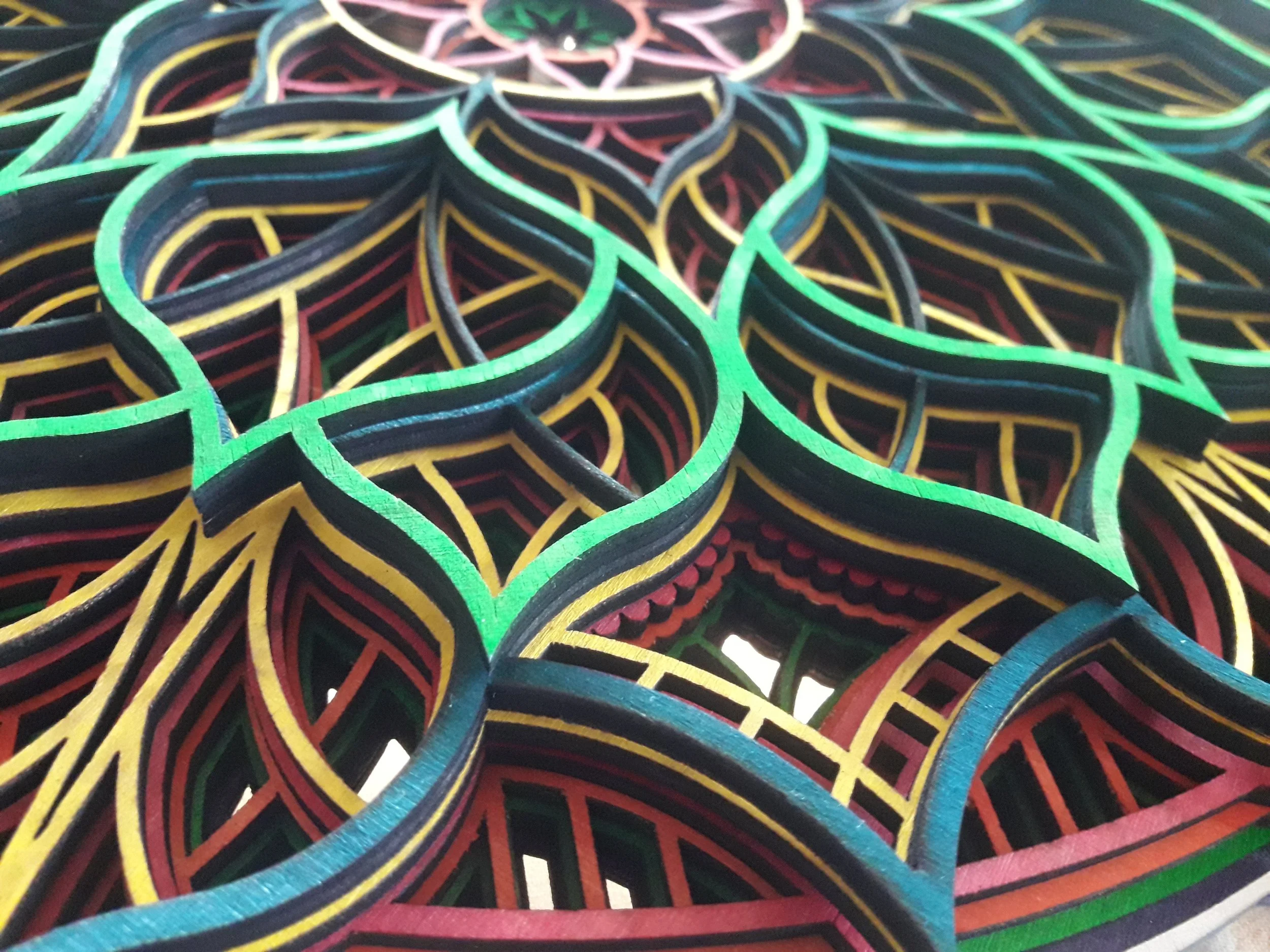 Multicolored geometric wooden cutout design resembling a mandala with red, green, and yellow patterns.