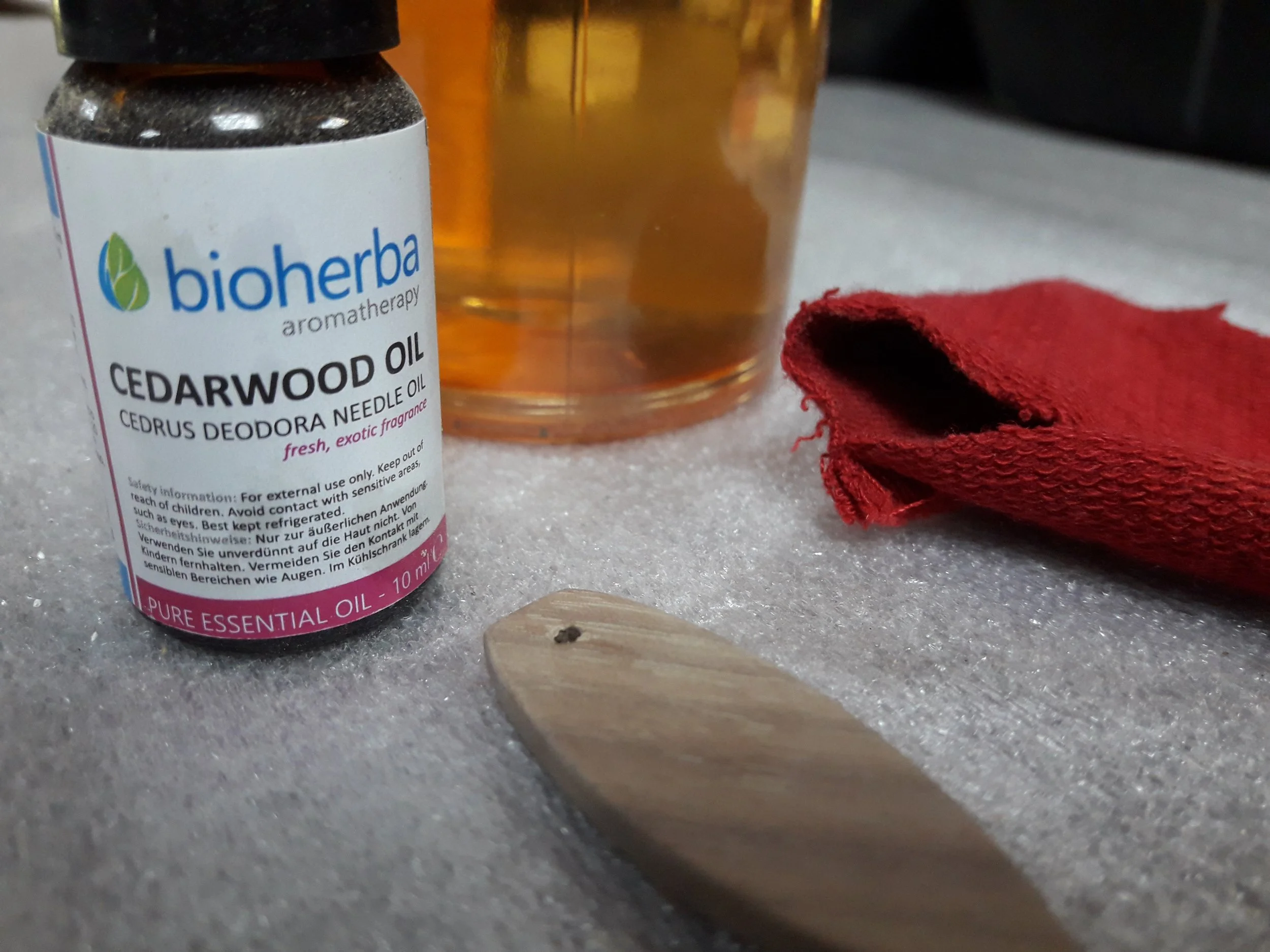 Cedarwood essential oil bottle labeled "bioherba" near a glass jar, red cloth, and wooden object on a table.