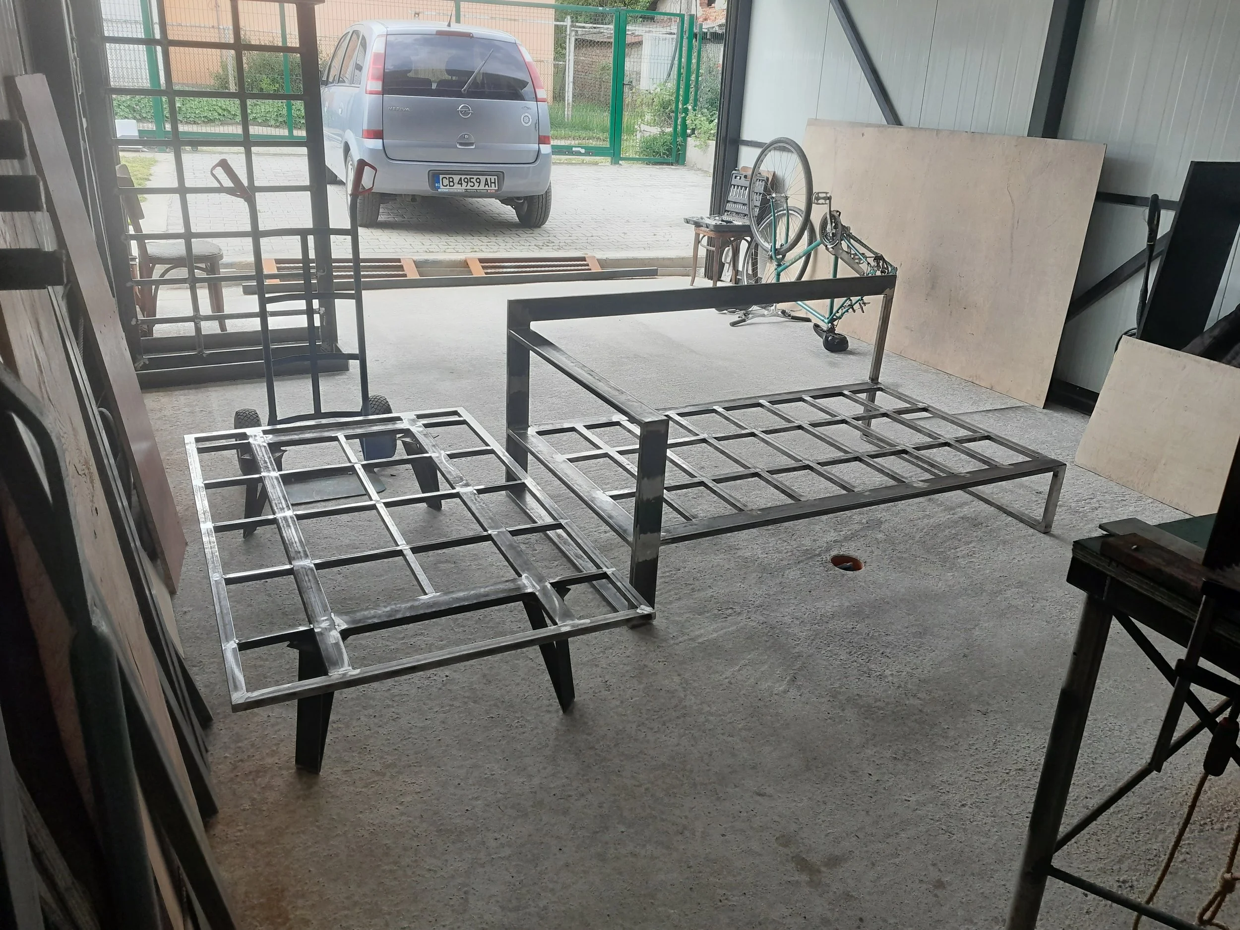Metal bed frames and a dolly in a garage or workshop, with a parked car and a bicycle in the background.