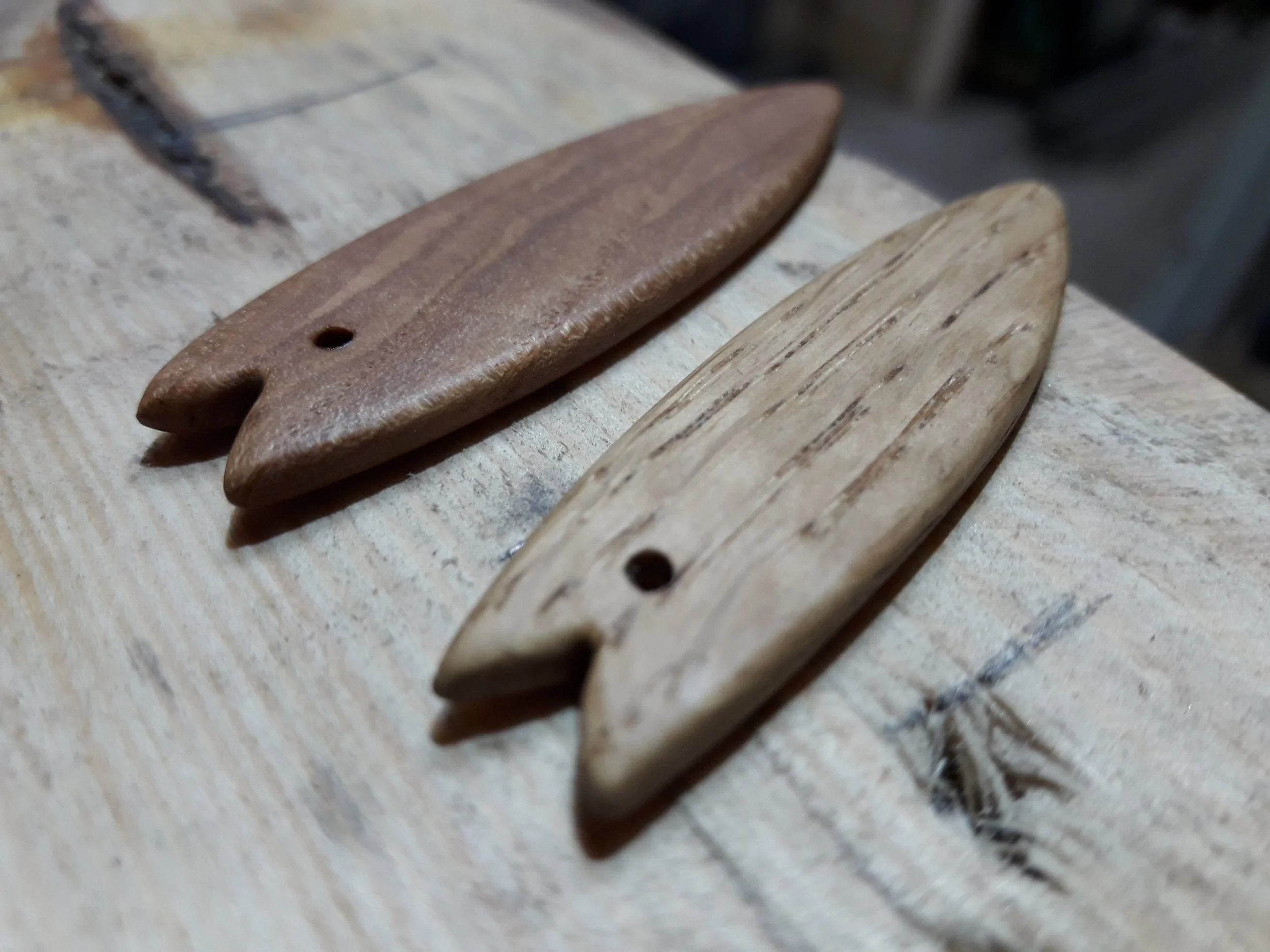 Two small wooden surfboard-shaped keychains with notched tails, placed on a wooden surface.