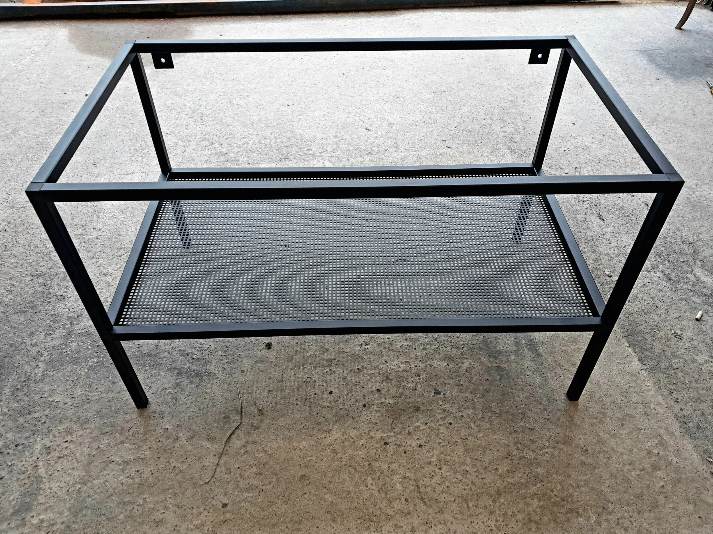Metal frame structure with a perforated metal shelf, possibly a part of furniture or a storage unit, on a concrete floor.