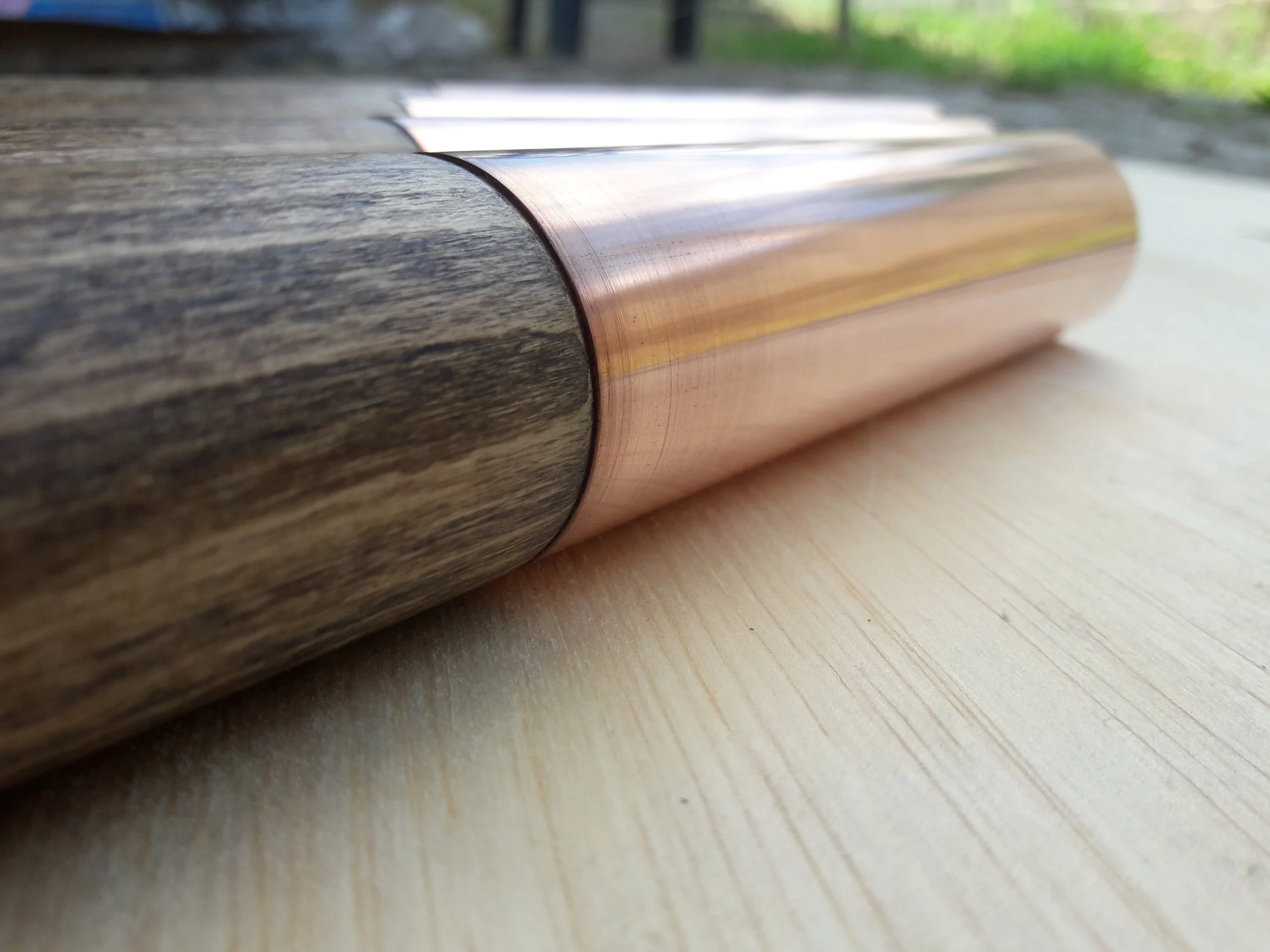 Close-up of a wooden cylindrical object with a copper or metallic section on a light wood surface.