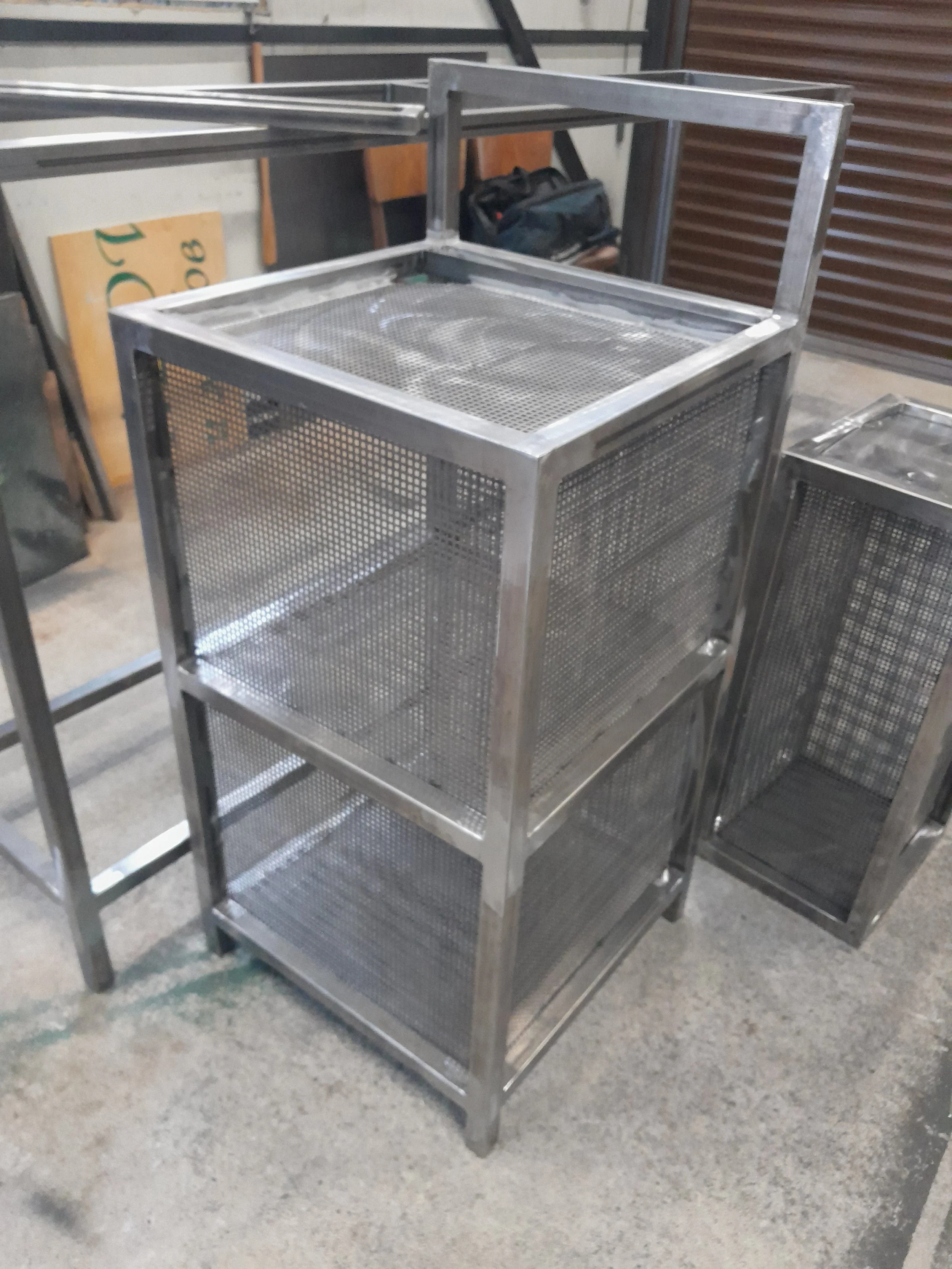 Metal wire mesh cage with a rectangular frame in a workshop setting.