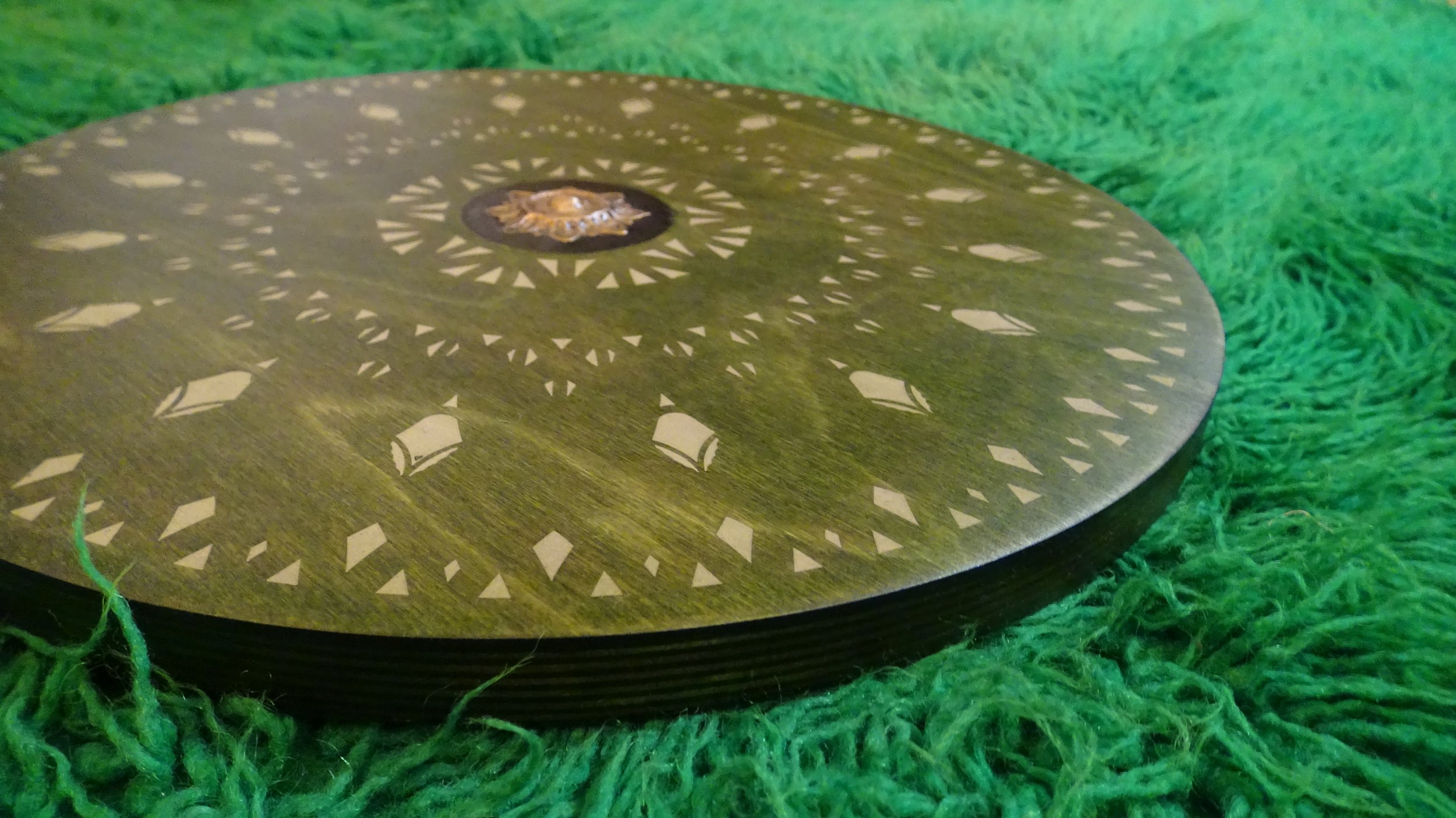 Decorative round wooden disc with geometric patterns on green textured surface.