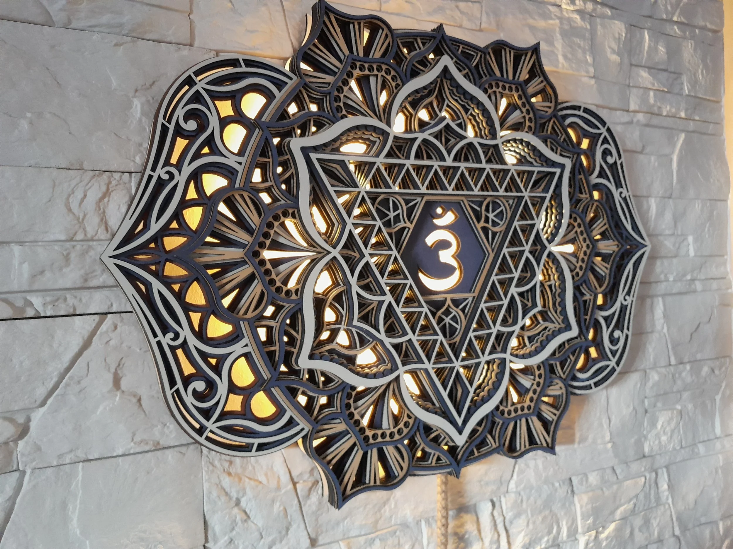 Geometric wall decor with intricate design and a central symbol, mounted on textured white stone.