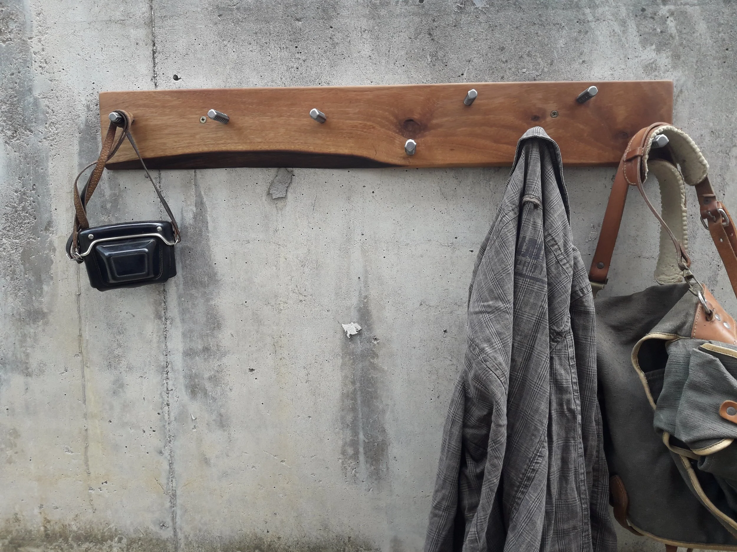 Wooden coat rack on concrete wall with camera case, jacket, and bag hanging.