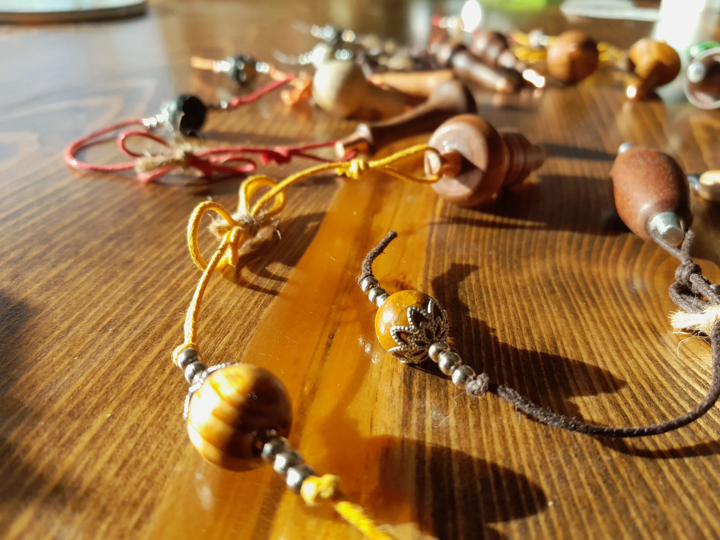 Assorted handcrafted jewelry on a wooden table, featuring beads and wooden elements with strings.