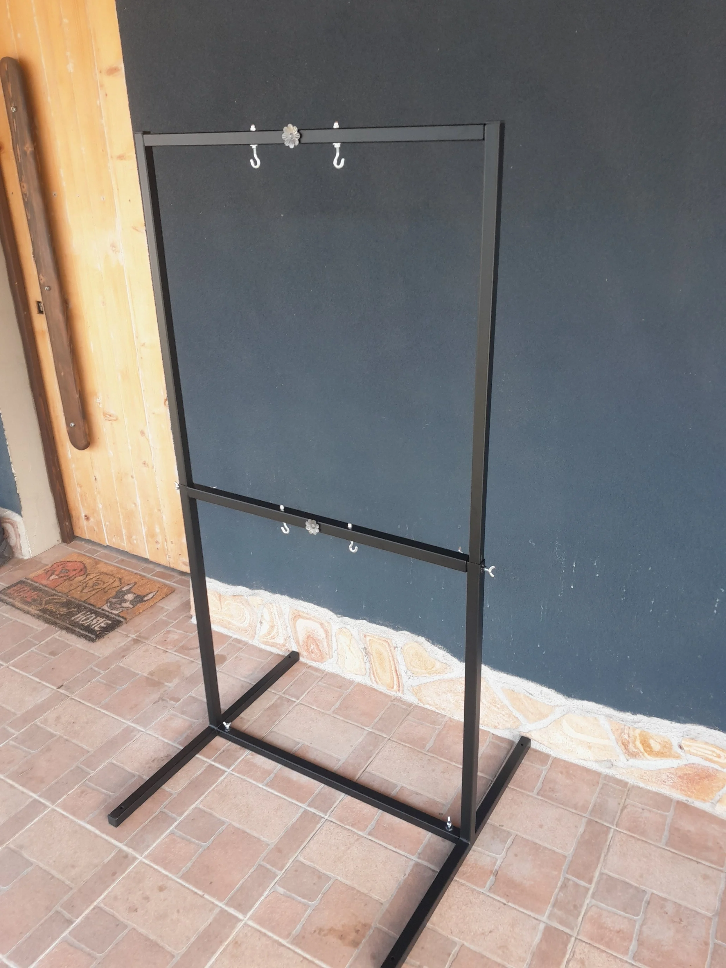 Metal frame stand with hooks, set against a dark wall, on a tiled floor.