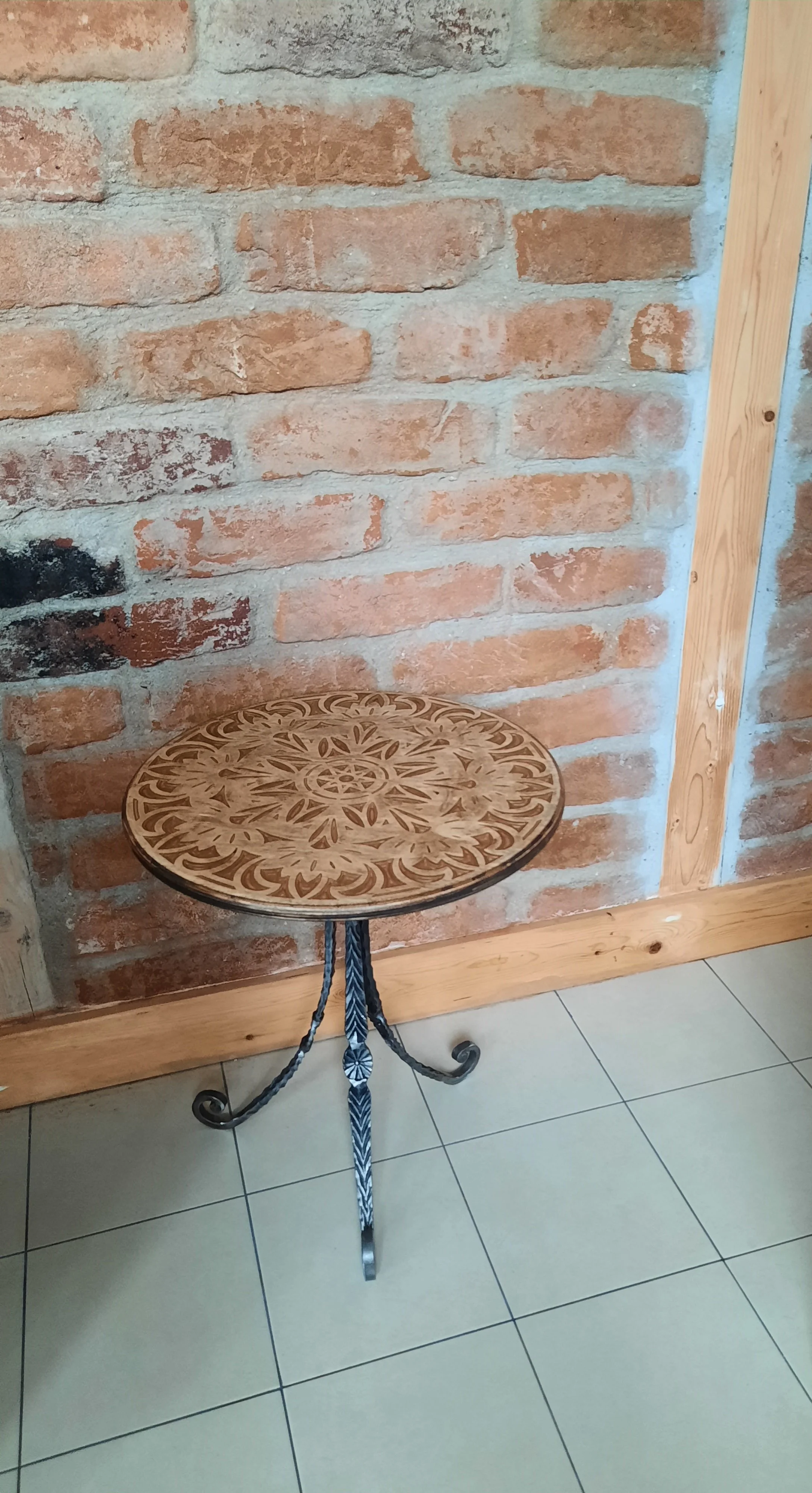 Decorative round side table with metal legs against brick wall