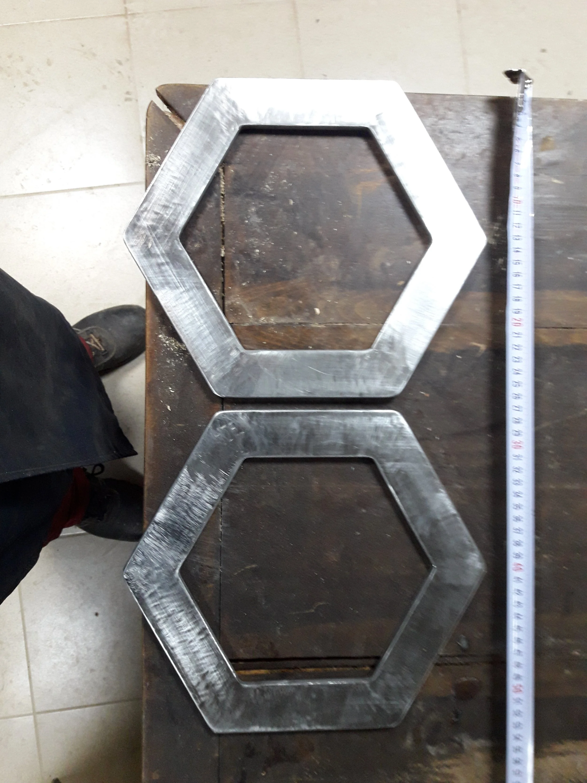 Two hexagonal metal frames on a workbench next to a measuring tape