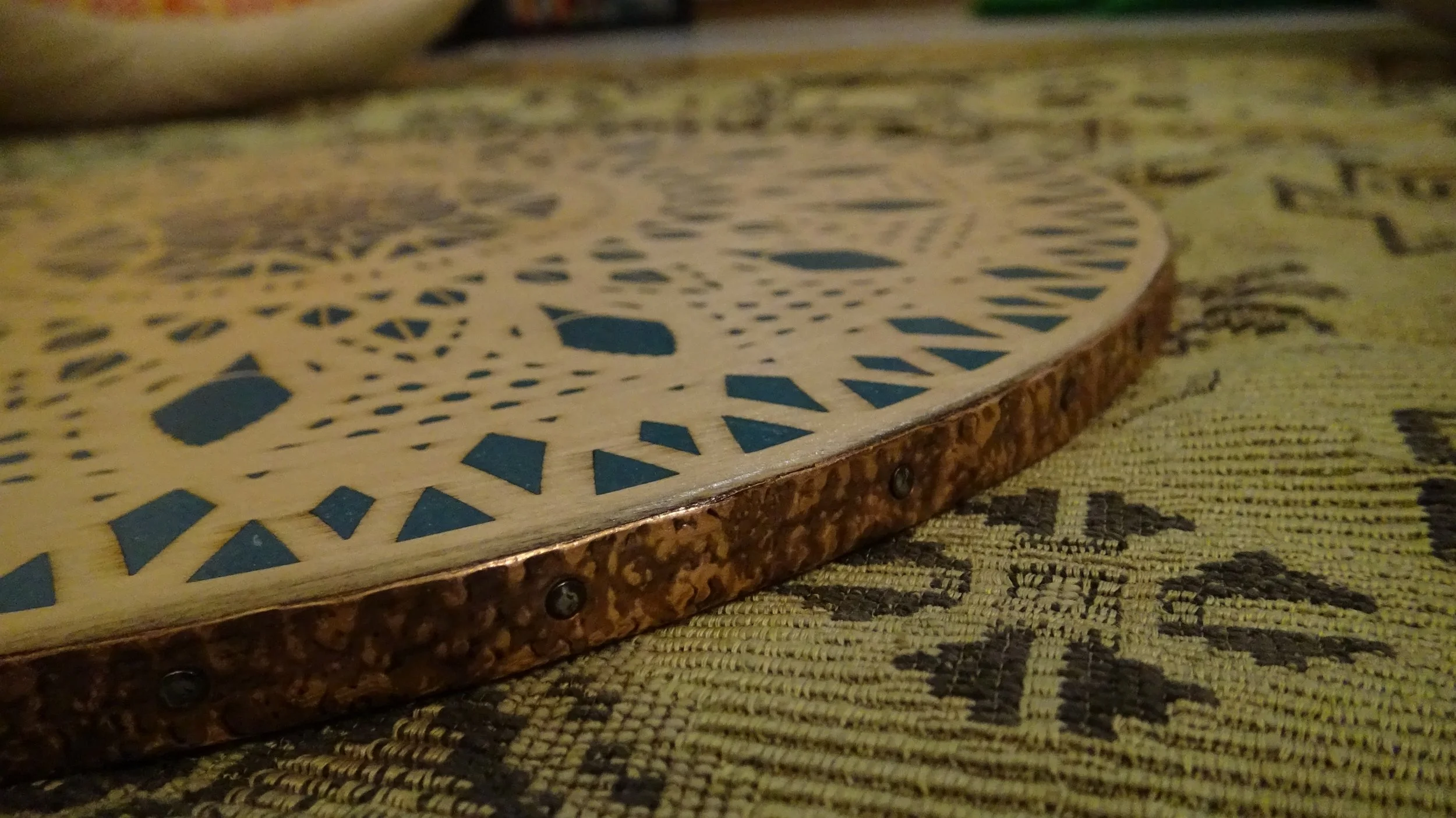 Close-up of a decorative wooden surface with blue geometric patterns and a textured metallic rim.