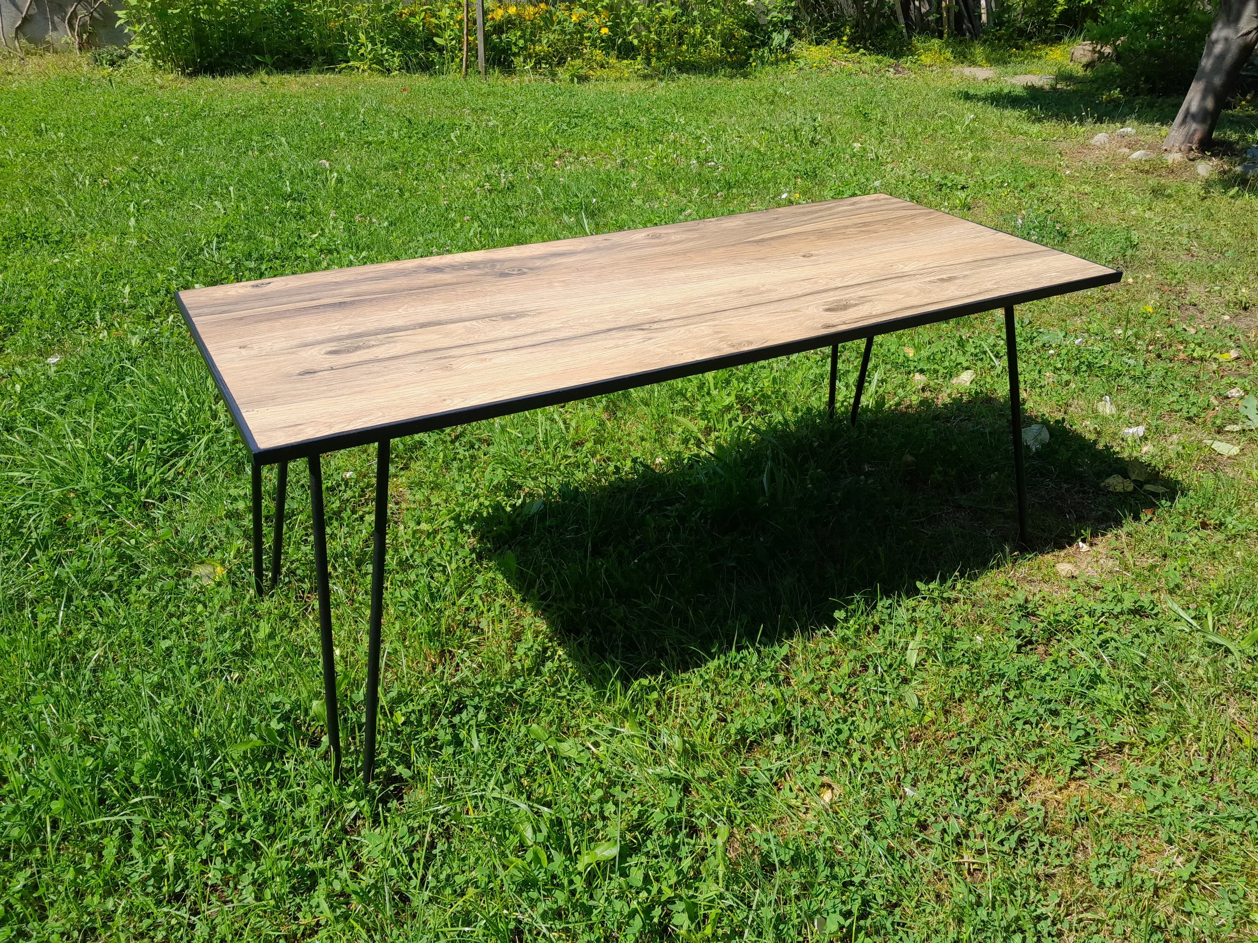 Wooden table with metal legs in a grassy outdoor setting.