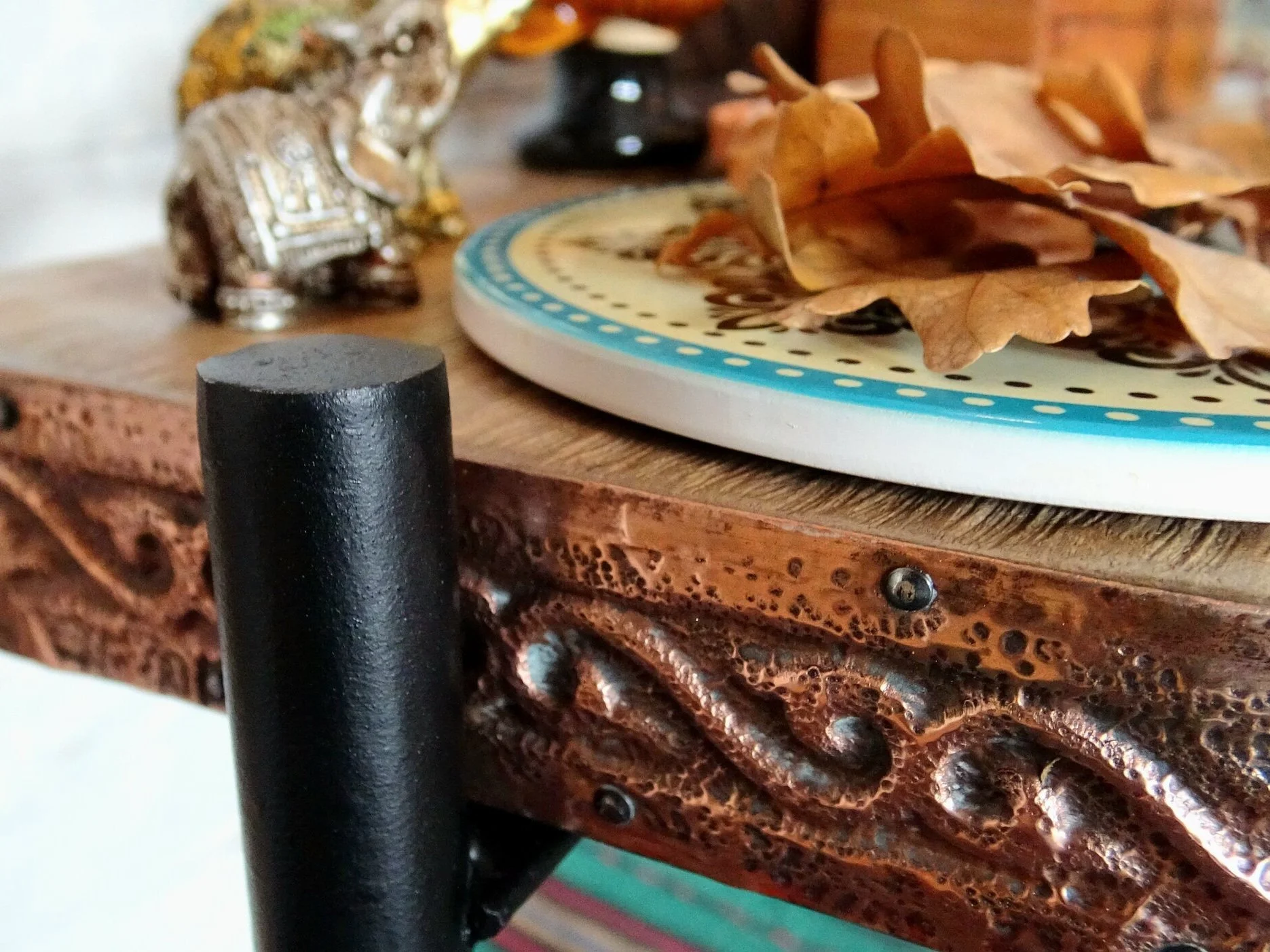 Close-up of a wooden shelf with decorative metal trim, featuring a small elephant figurine, a decorative plate, and dried leaves.
