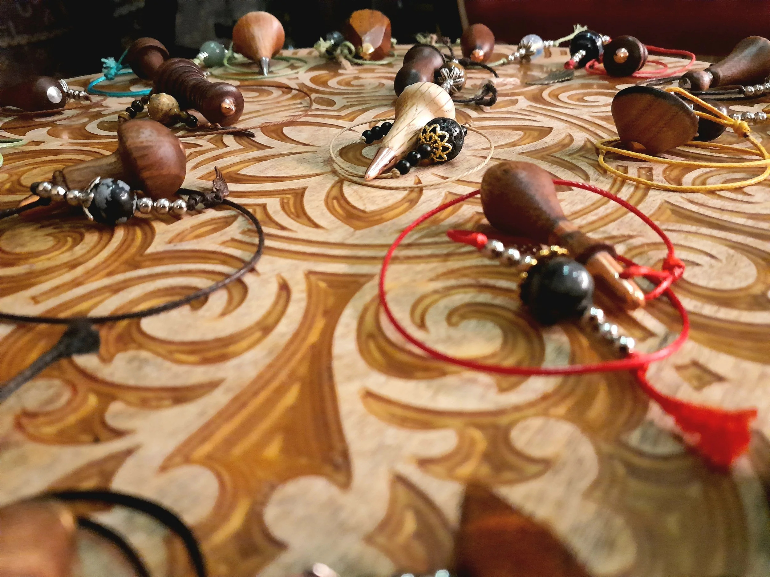 A collection of wooden pendulums with beads, strings, and decorative details on an ornate wooden surface.