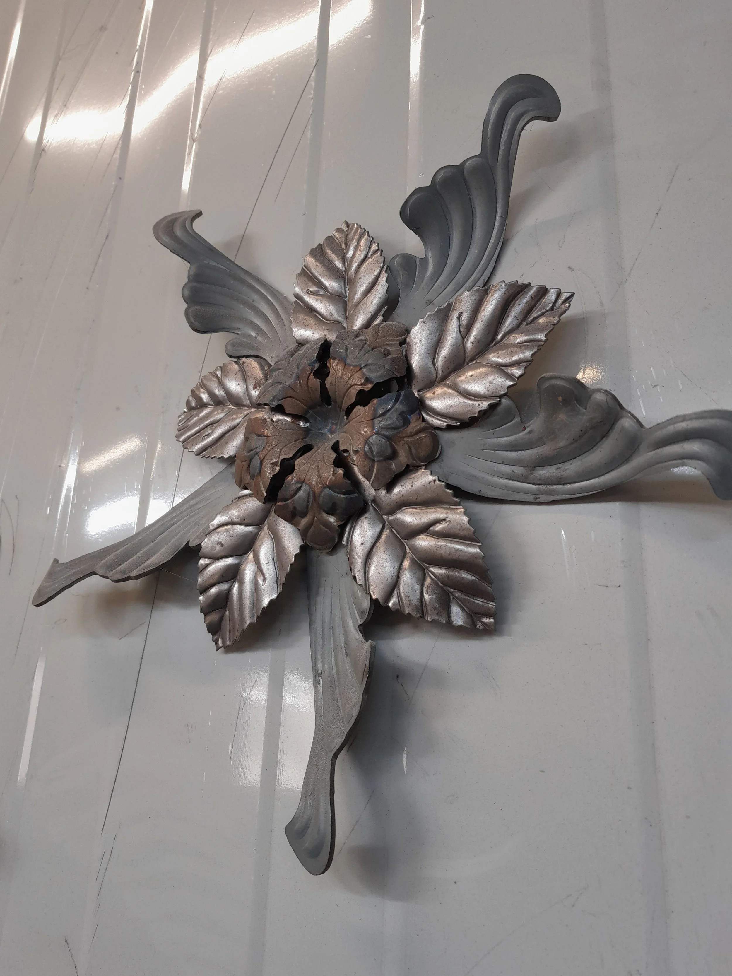 Decorative metal wall art with floral design, featuring leaves and intricate patterns, mounted on a wall.