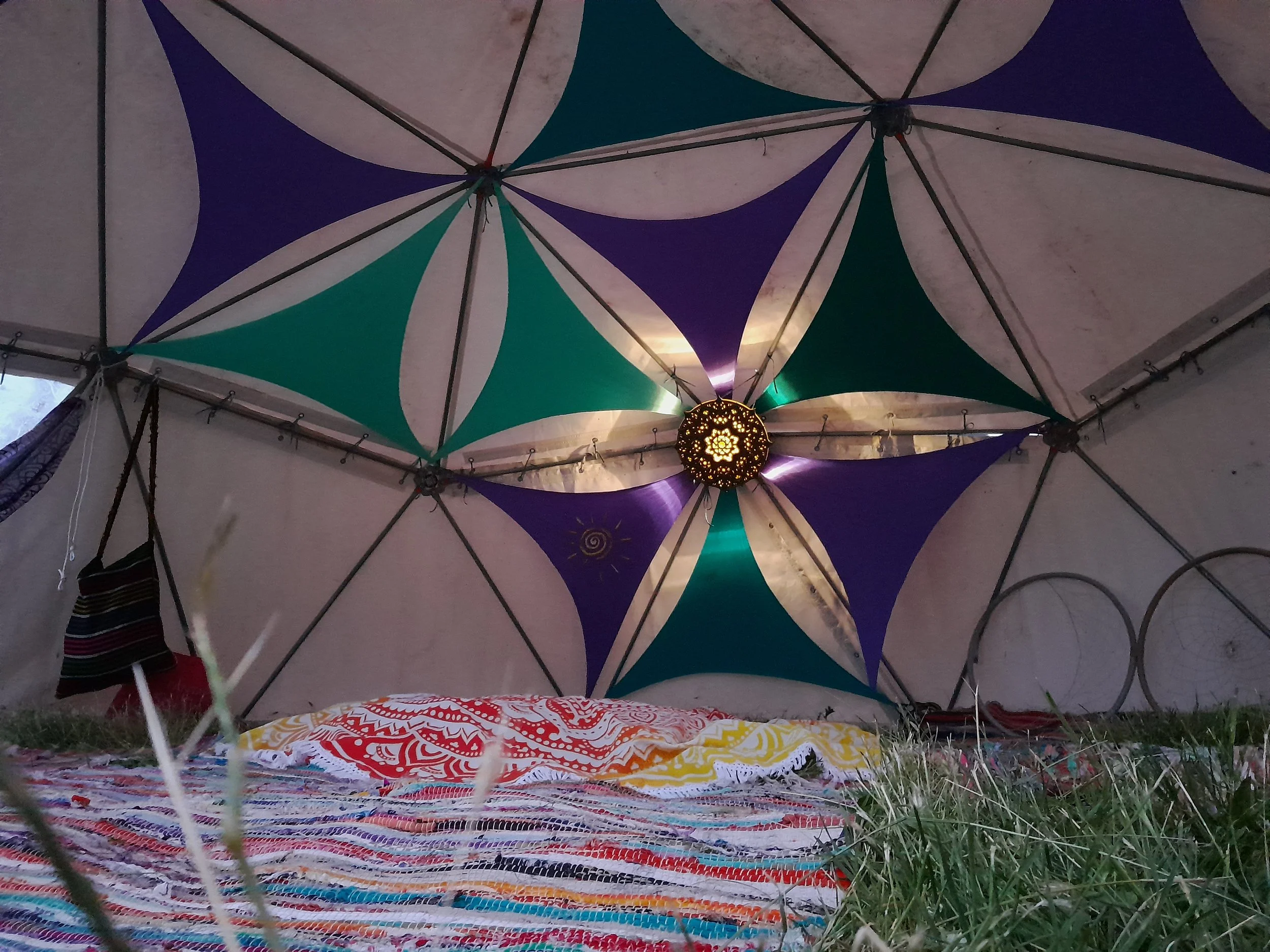 Inside a geodesic dome with colorful star pattern and central light, featuring a striped bag and patterned rug on the ground.