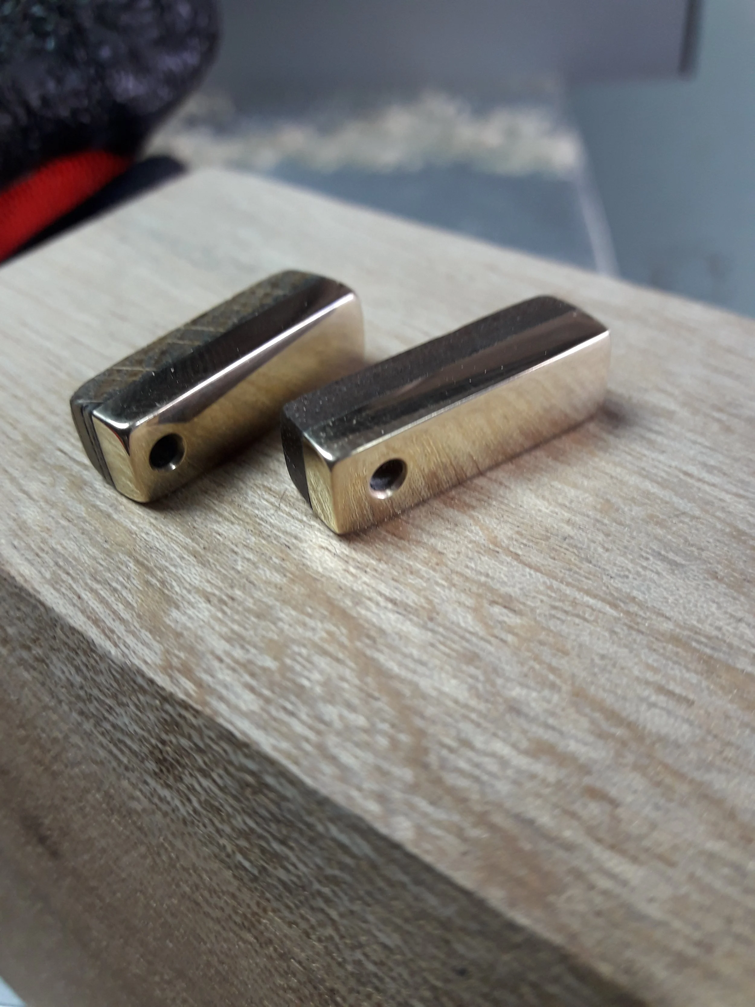Two rectangular metal blocks with holes on a wooden surface.