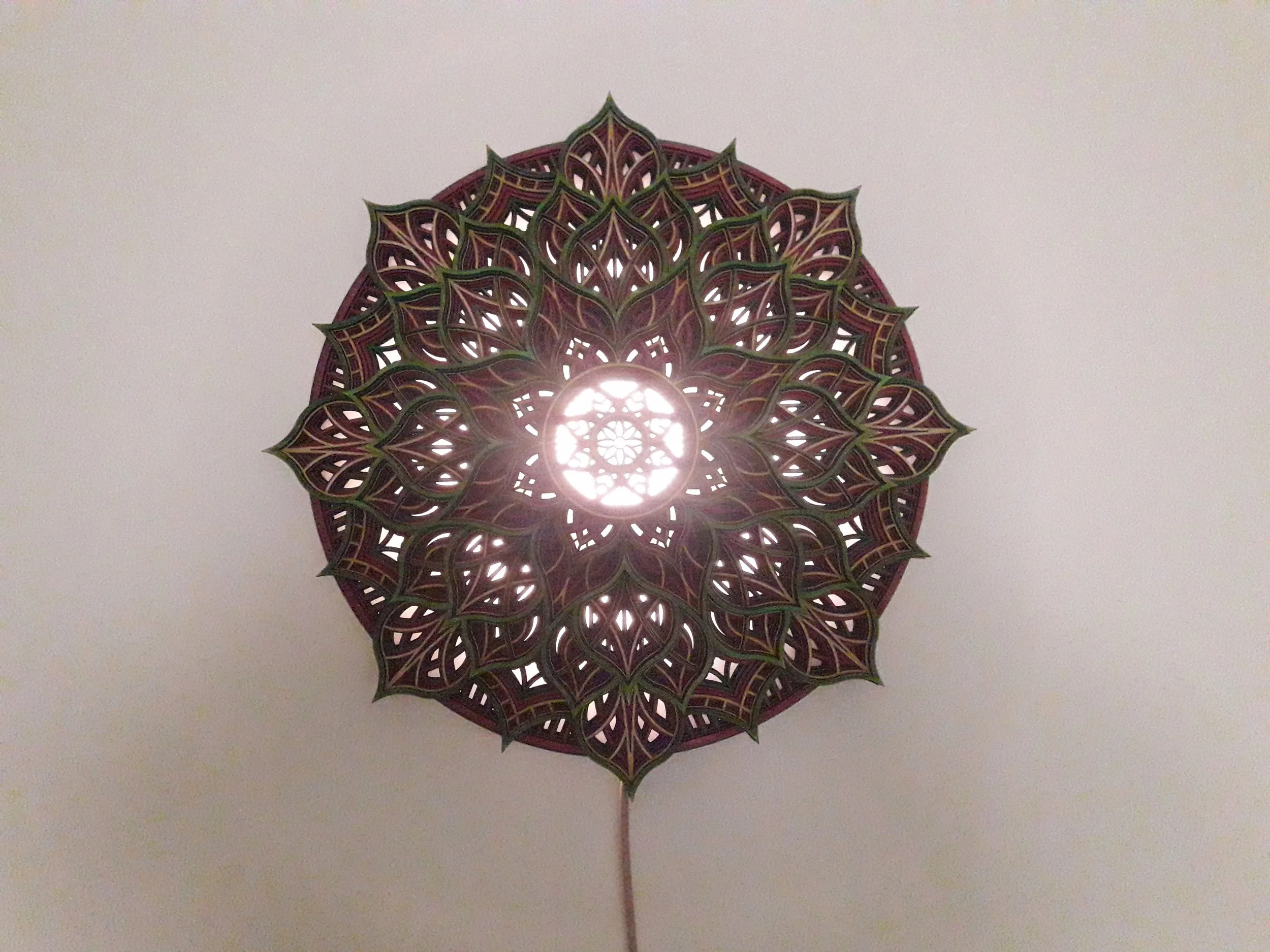 Intricate mandala-style lamp with layered cutout design and central light source on a white background.