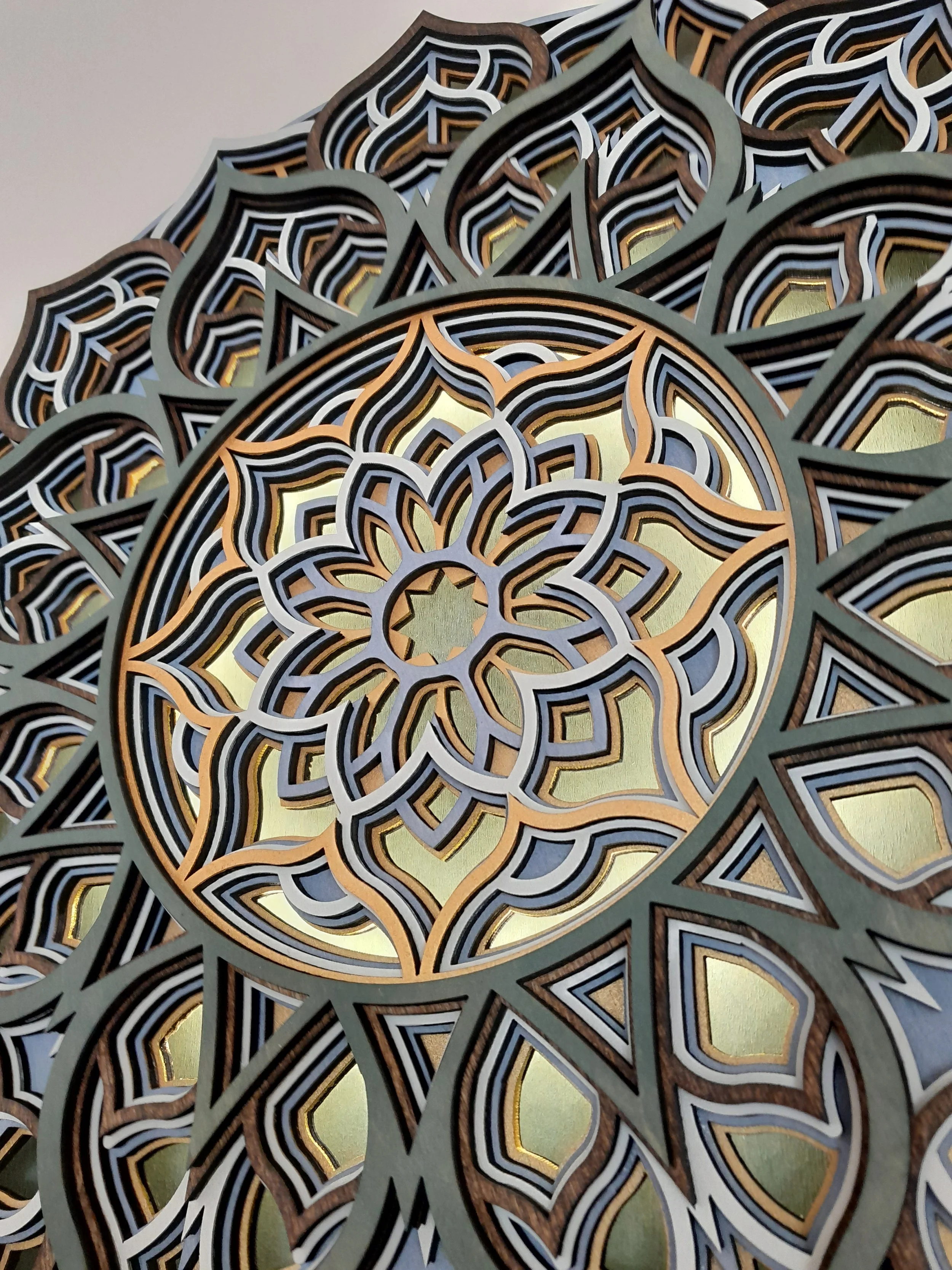 Intricate layered mandala pattern with geometric shapes in shades of gold, blue, and brown, creating a three-dimensional effect.