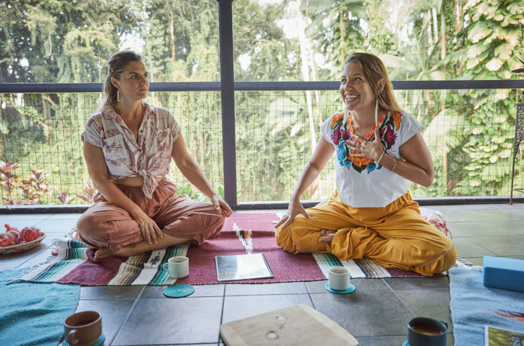 People around a wooden table with fresh herbs, a knife, plates, and cups, preparing food.
