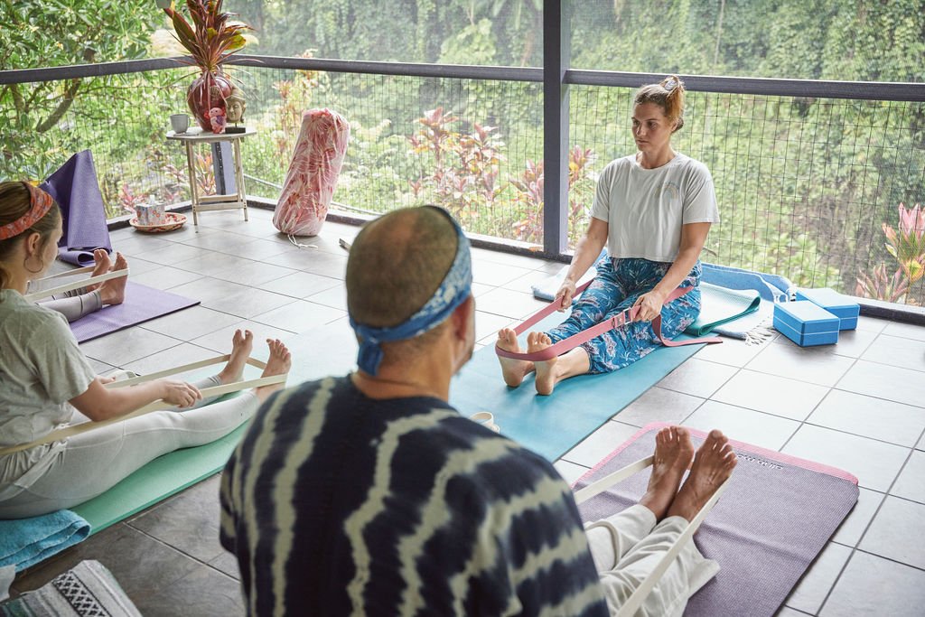 Person in a patchwork skirt standing on rocks near the ocean with arms outstretched.