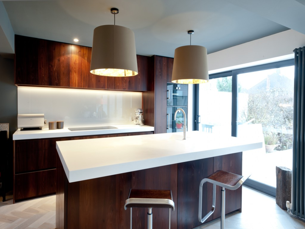 Modern kitchen with white island and dark wood cabinetry, two large pendant lights, and a large sliding glass door showing a snowy outdoor scene.