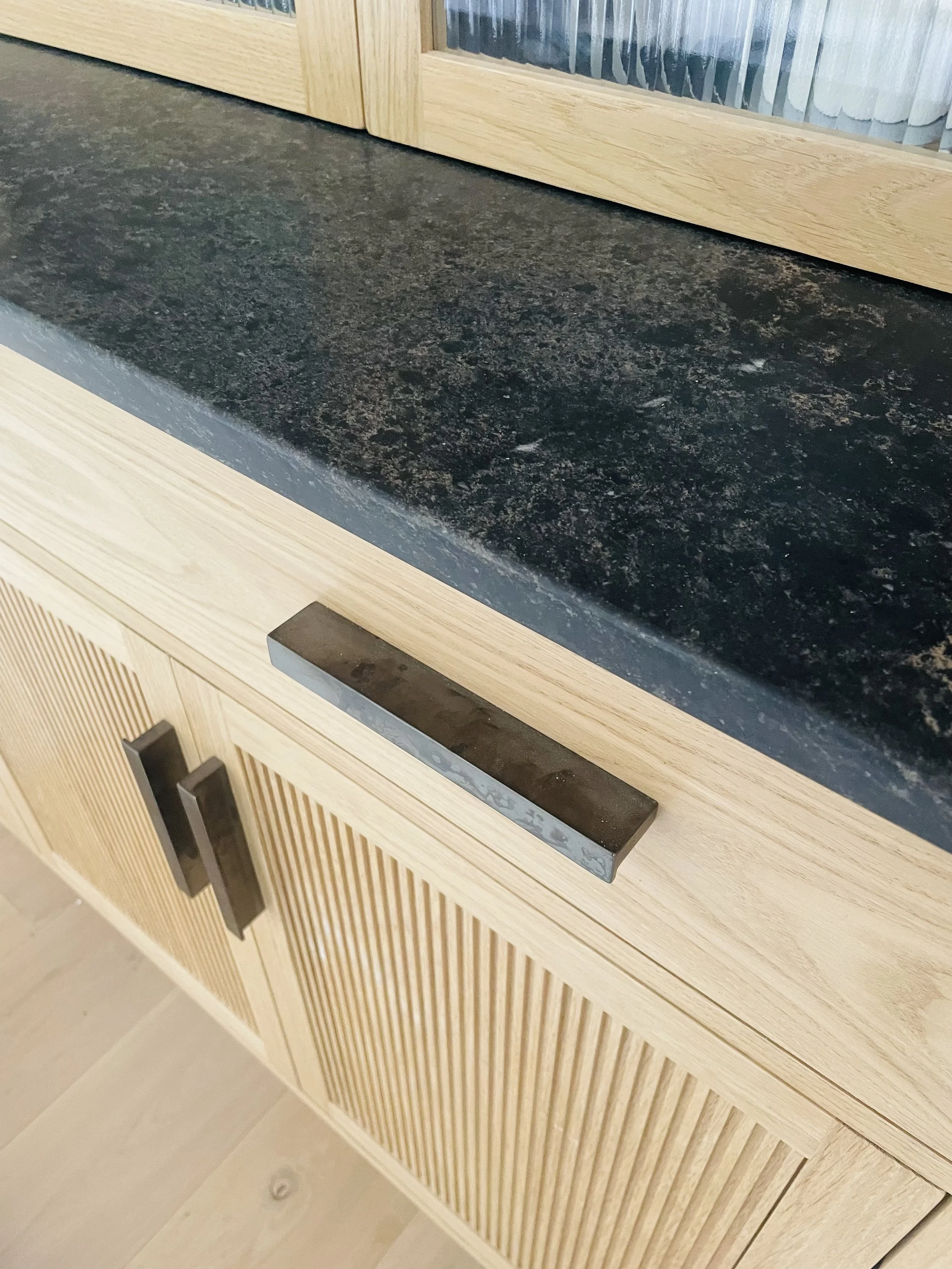 Close-up of a kitchen or cabinet drawer with a textured black countertop above and wooden cabinet doors below, featuring modern black handles.