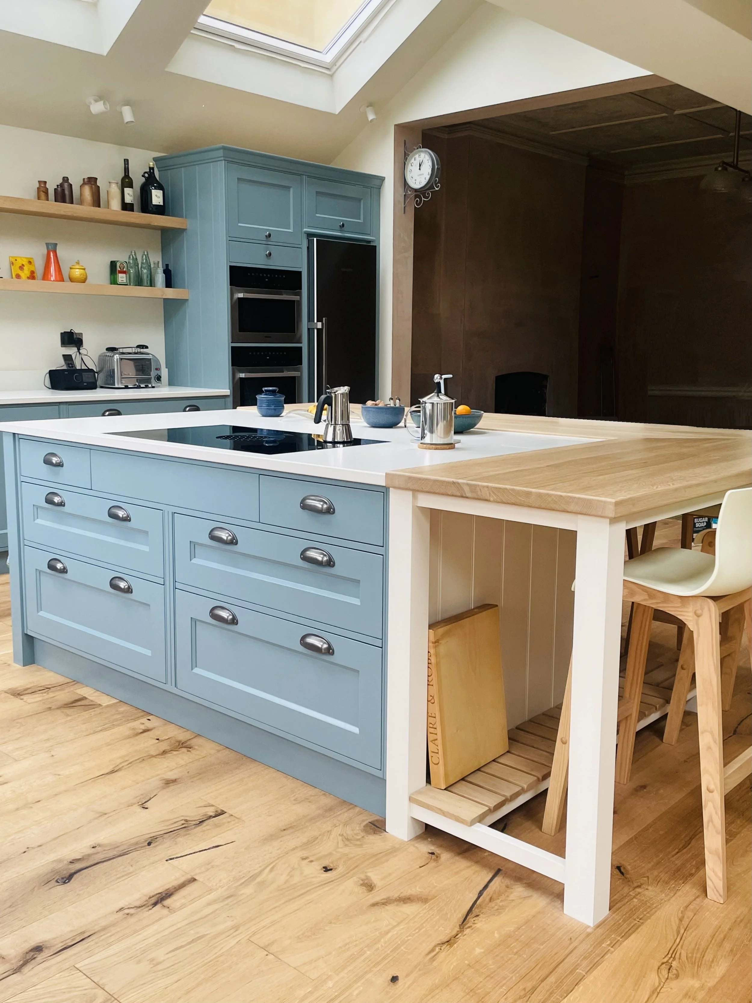 Modern kitchen with light blue cabinetry, wooden countertops, and a white and wood island, featuring a skylight overhead and a wall clock.