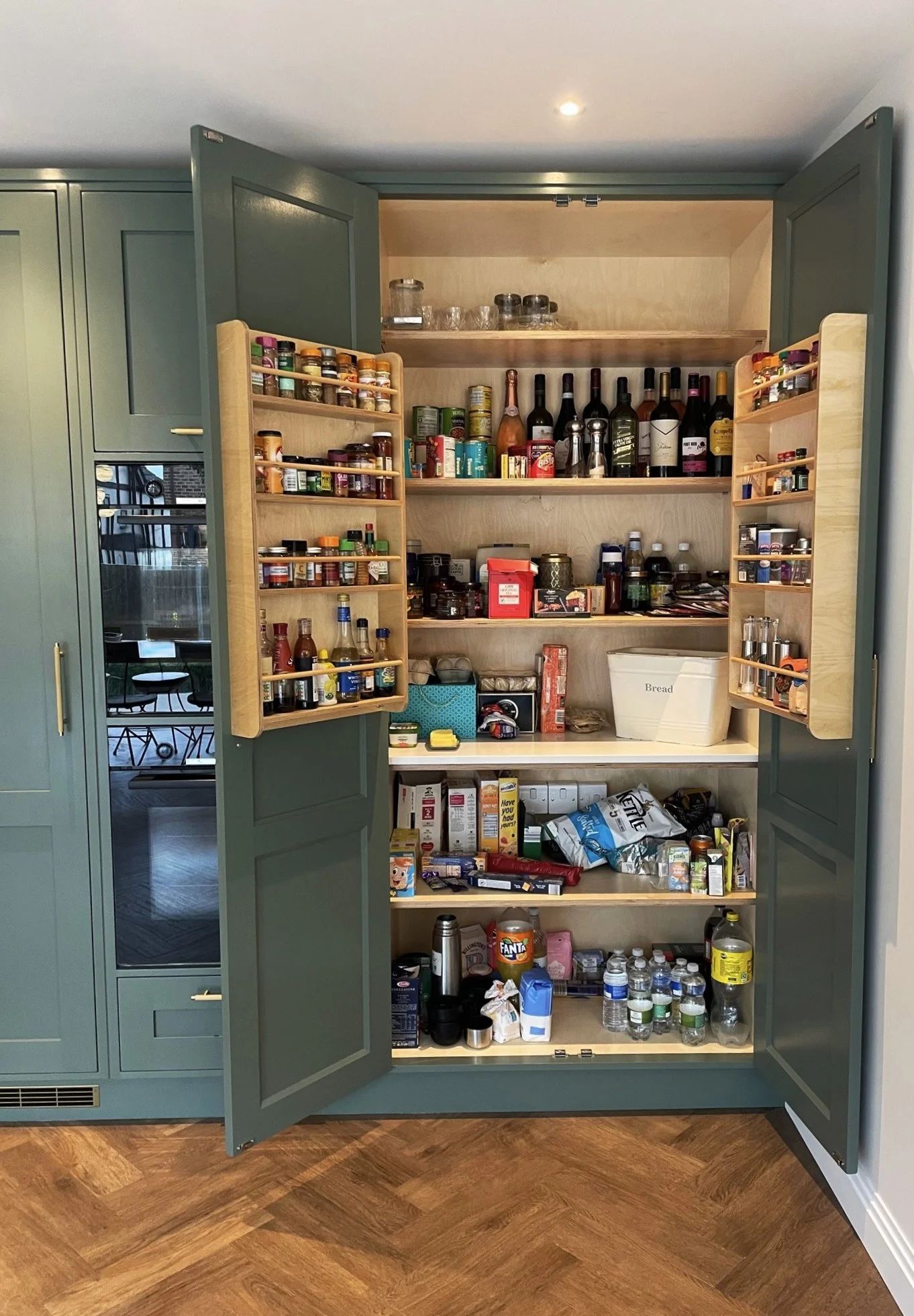 Open kitchen cabinet filled with spices, jars, bottles, snacks, and bottled water. The cabinet has multiple shelves and pull-out spice racks.