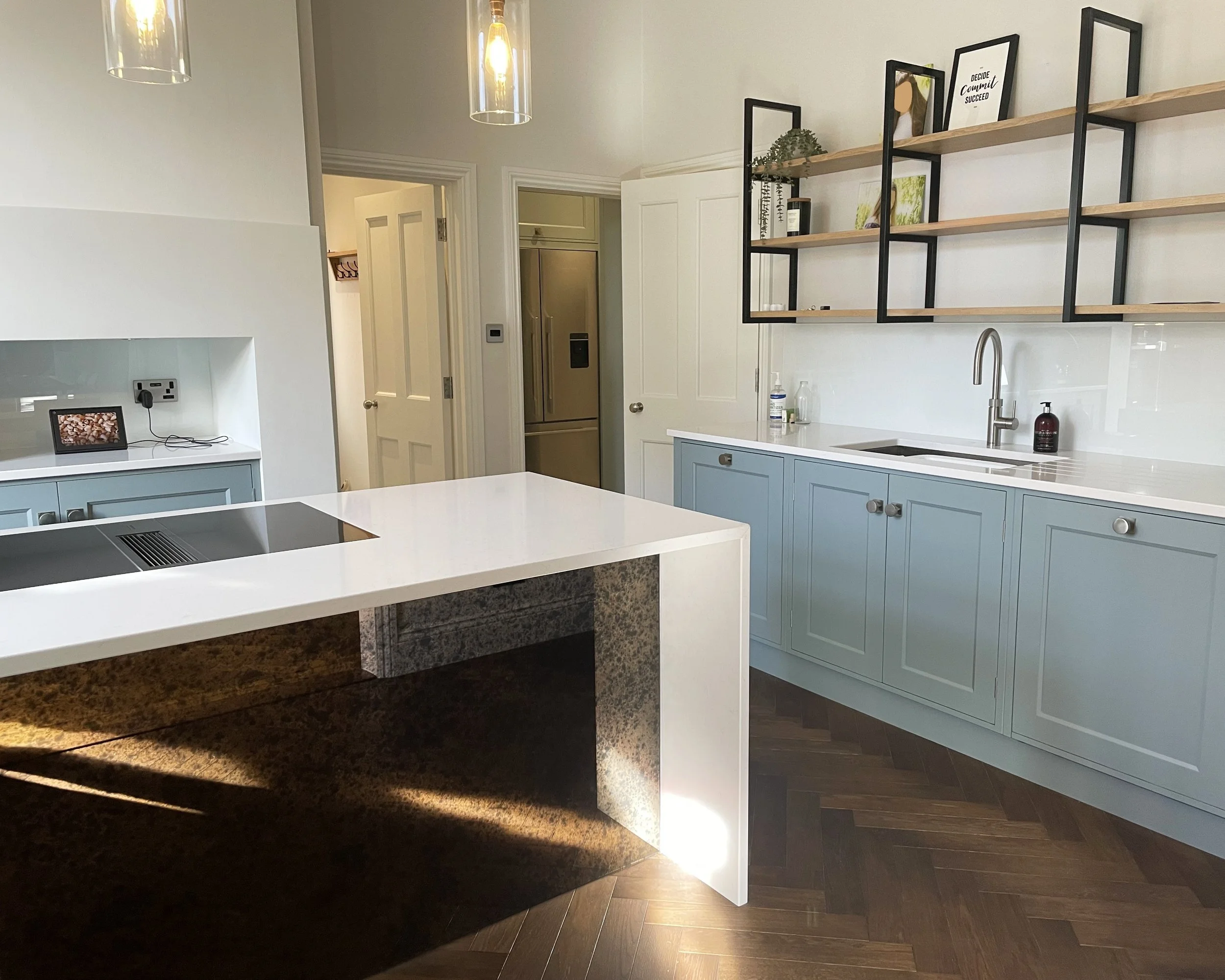 Modern kitchen with light blue cabinets, wooden open shelves, white countertop, and two pendant lights.
